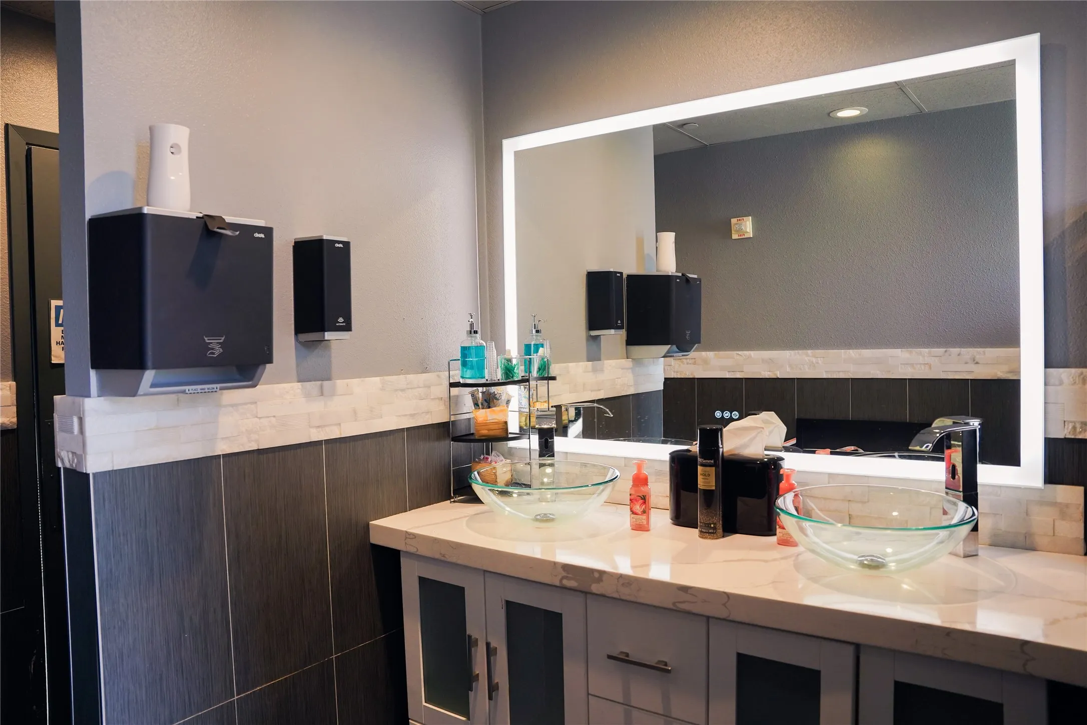 Vanity with dual glass vessel sinks, stone-finish countertop, and integrated lighted mirror