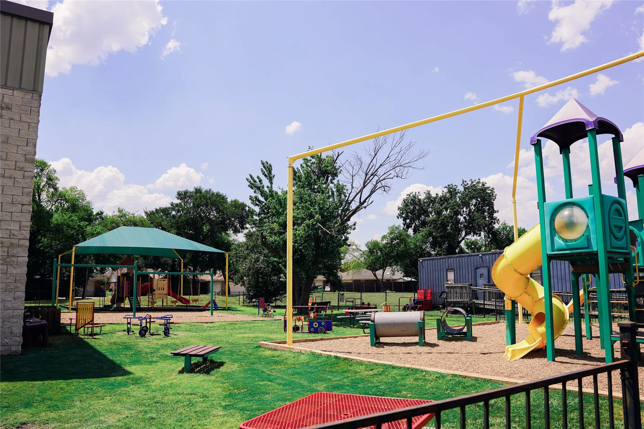 Expansive outdoor recreation area with natural grass, a large play structure featuring a spiral slide, a shaded play area, and additional playground equipment