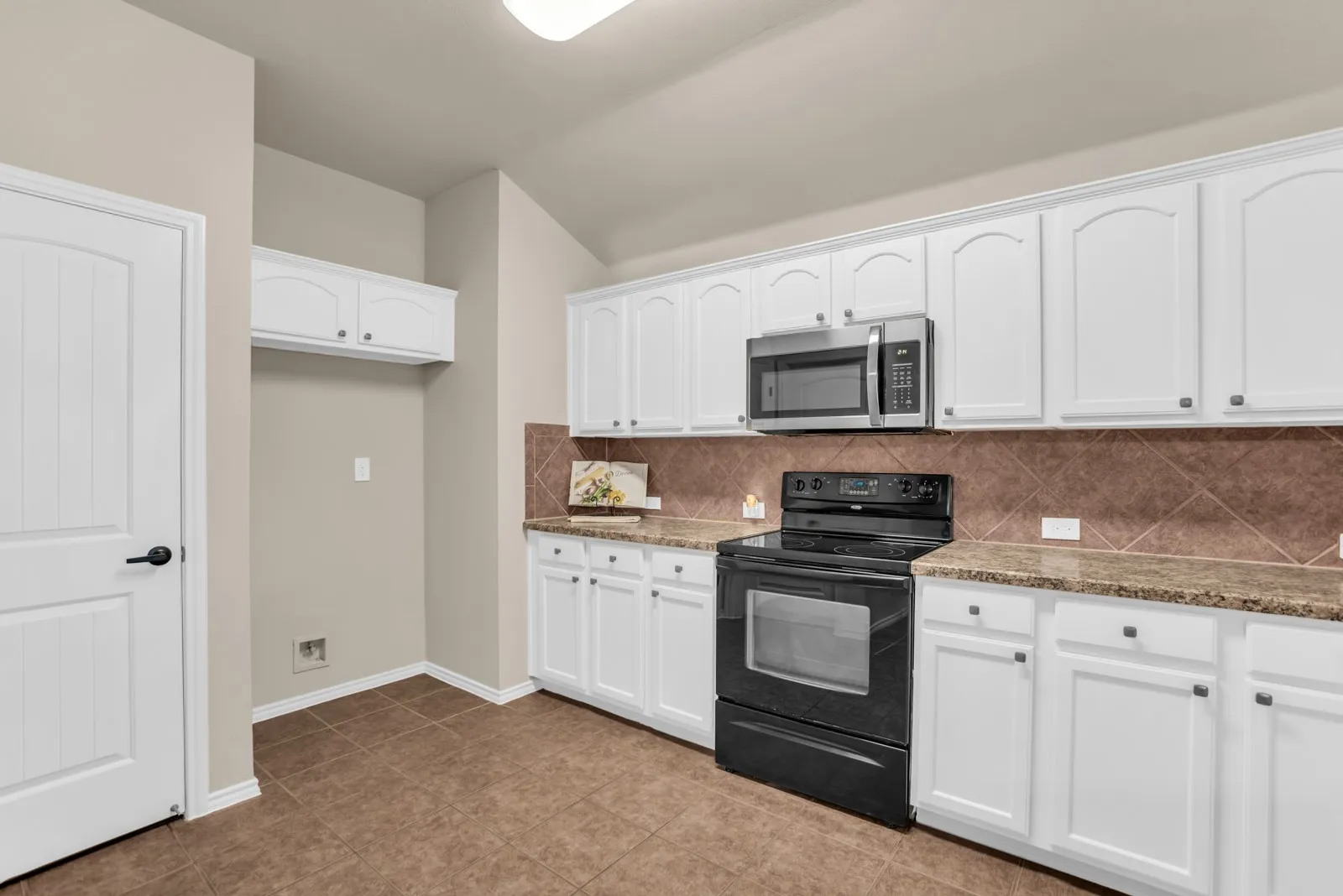 Kitchen featuring white cabinetry, stone-finish countertops, stainless steel microwave, black electric range, and tile flooring