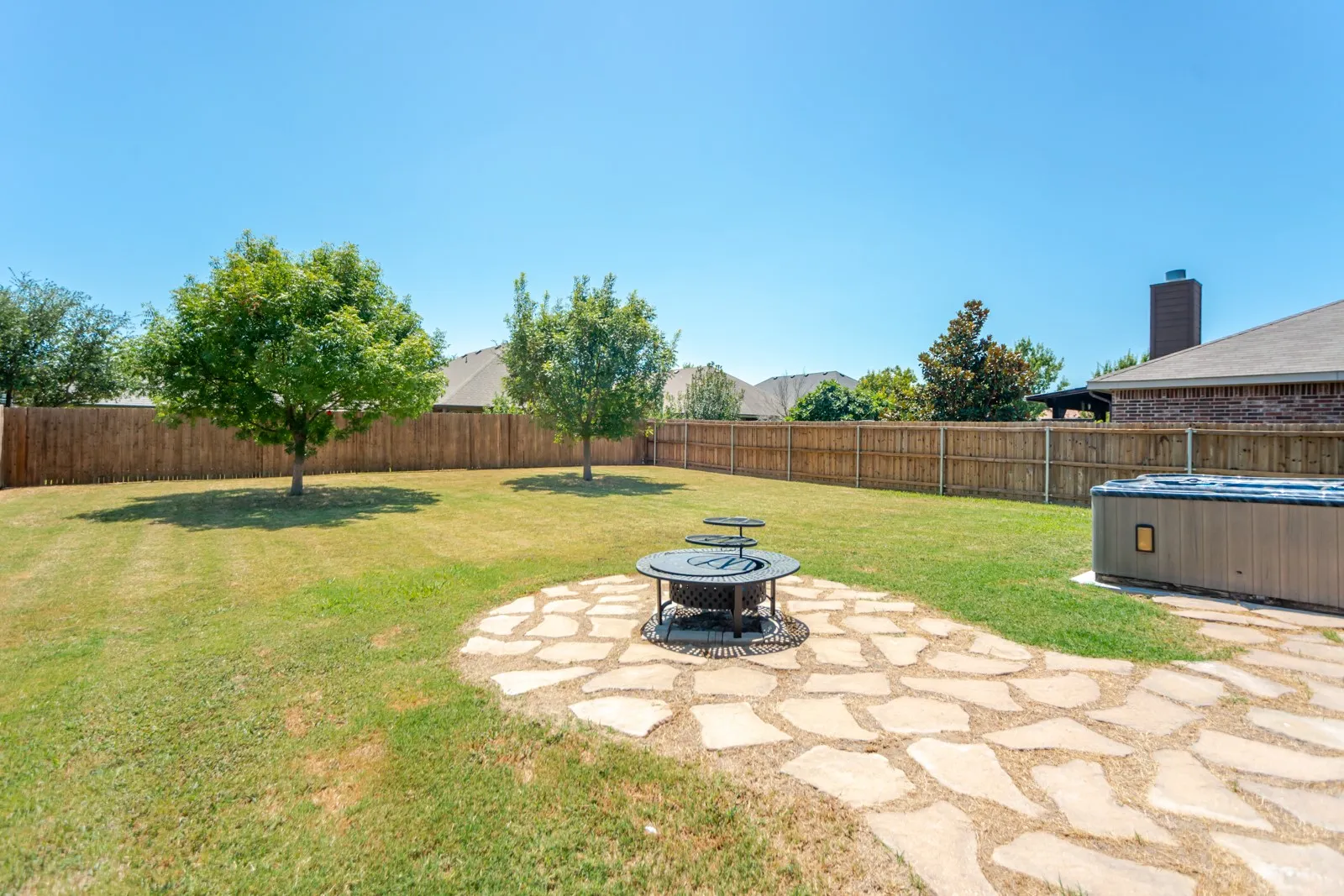 Spacious backyard with a wood privacy fence, flagstone patio, fire pit, and a hot tub