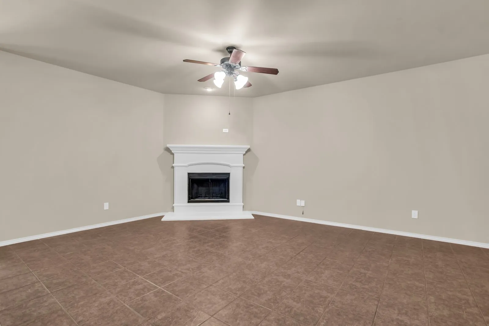 Spacious living room featuring a decorative fireplace with a white mantel, tile flooring, and a ceiling fan