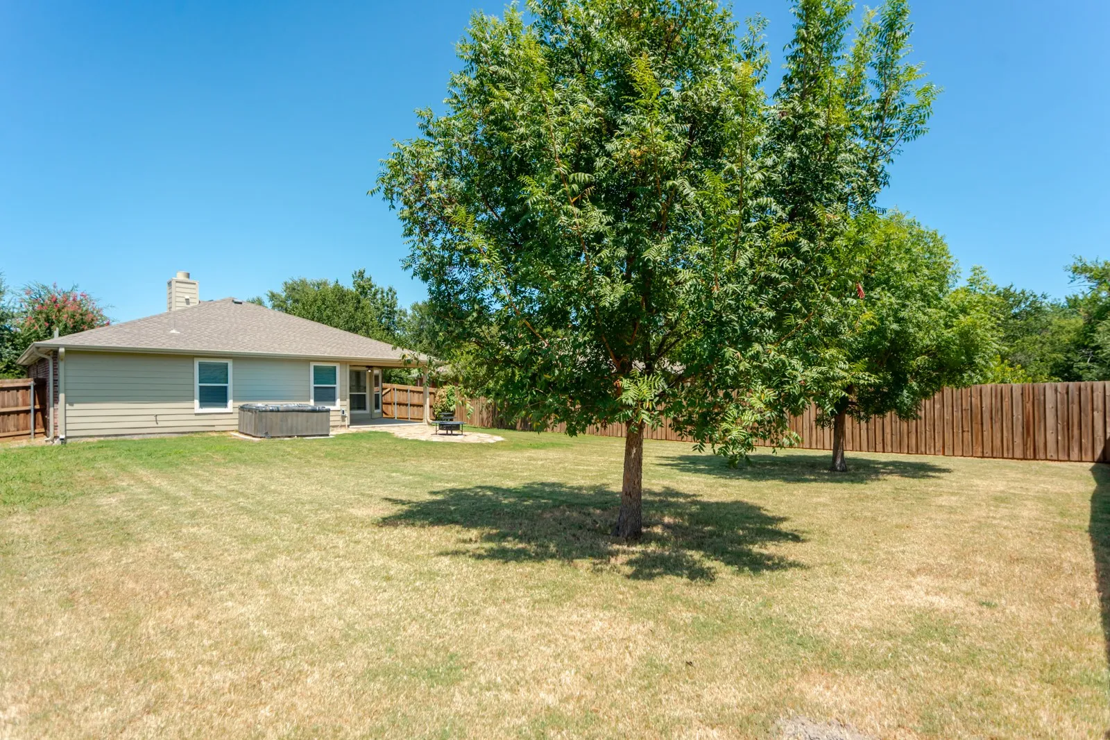 Expansive backyard with a covered patio, privacy fencing, and mature trees