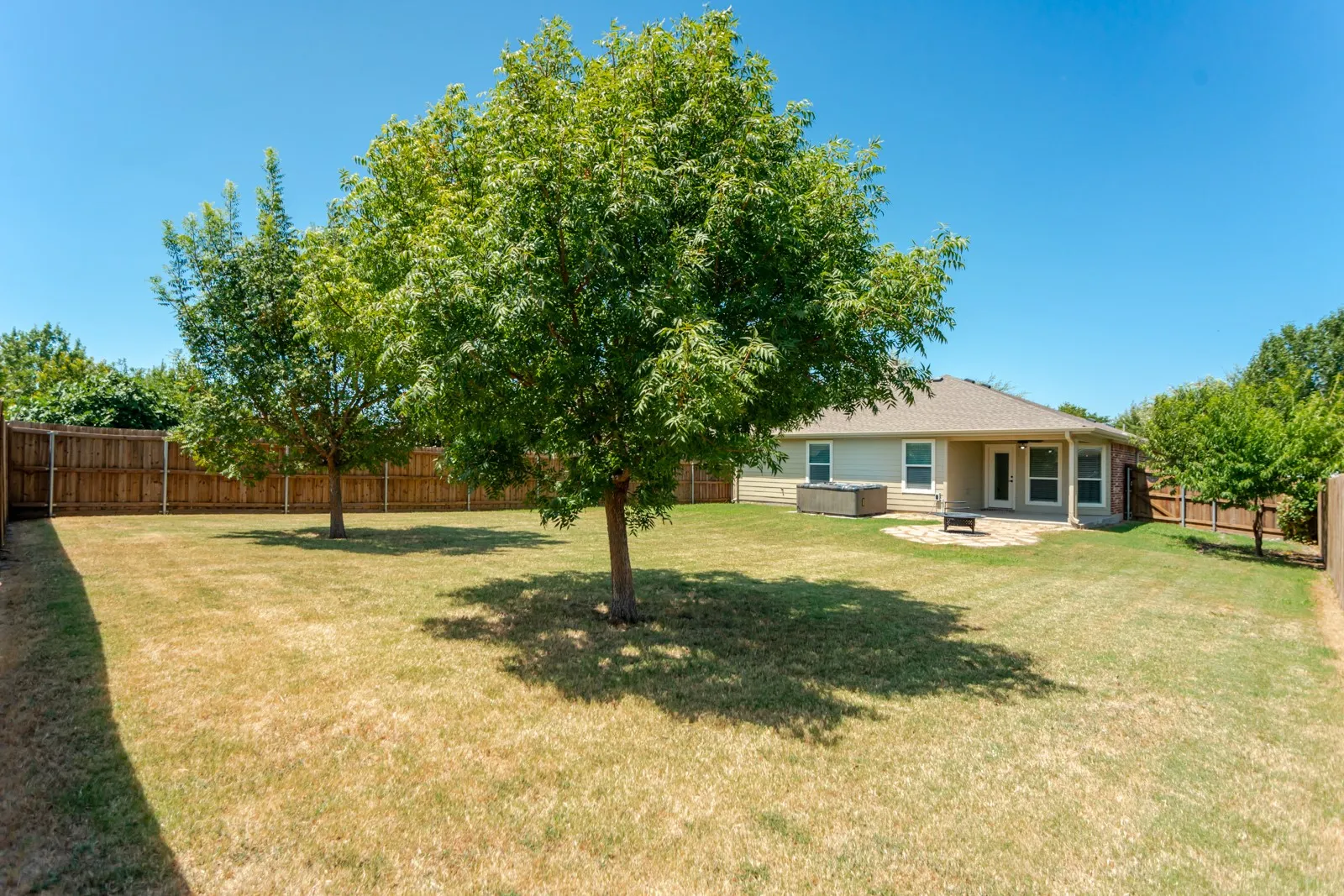 Fenced backyard with mature trees, a stone patio, and a covered patio area