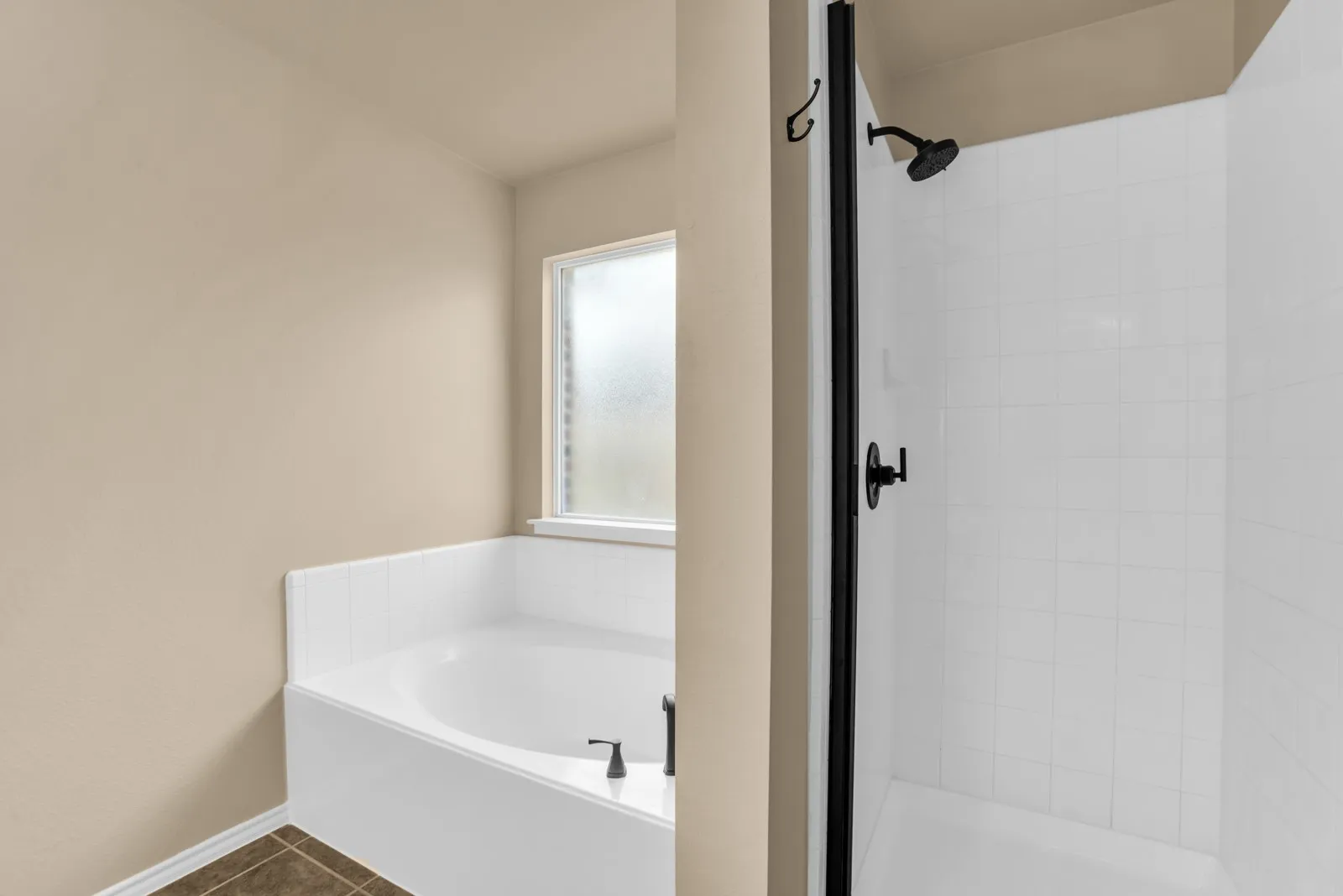 Built-in soaking tub with tile surround, frosted window, and black fixtures