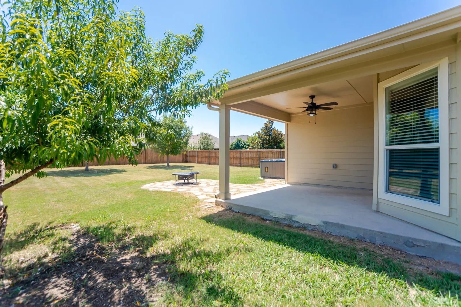 Covered patio with a ceiling fan, concrete flooring, and an expansive lawn featuring mature trees