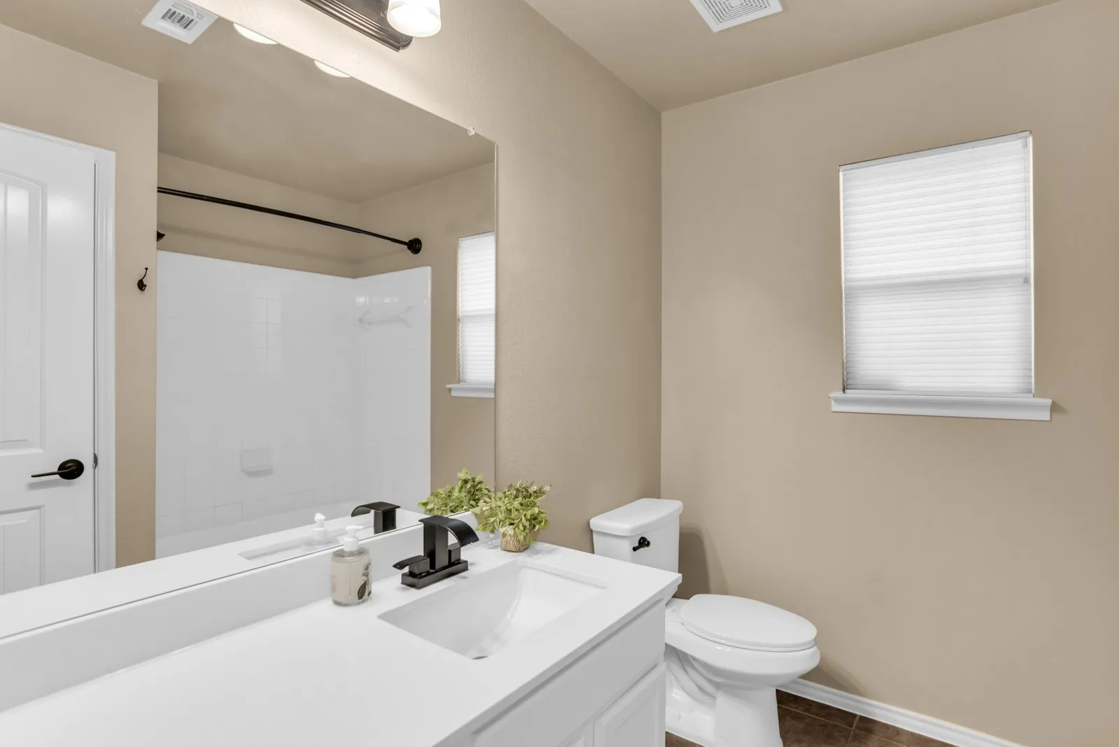 Bathroom featuring a white vanity with integrated sink, black fixtures, a wall-mounted mirror, white toilet, and a window with blinds. All updated.