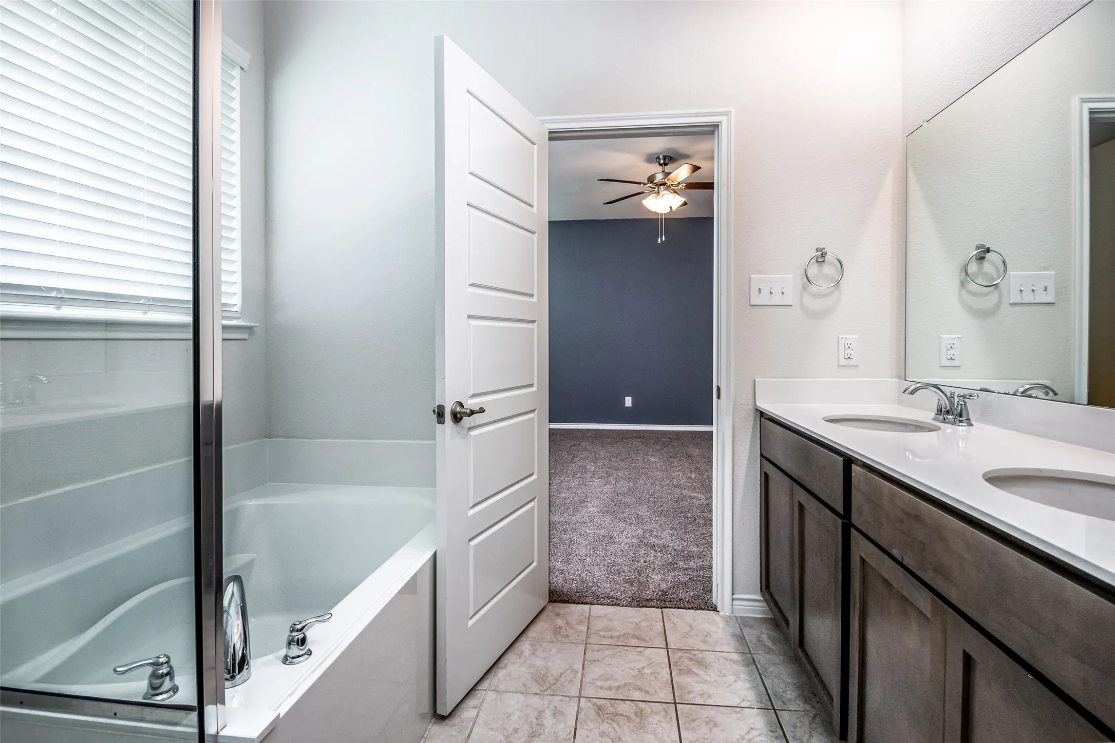 Dual vanity with undermount sinks and chrome fixtures, white countertops, and wood-finish cabinetry