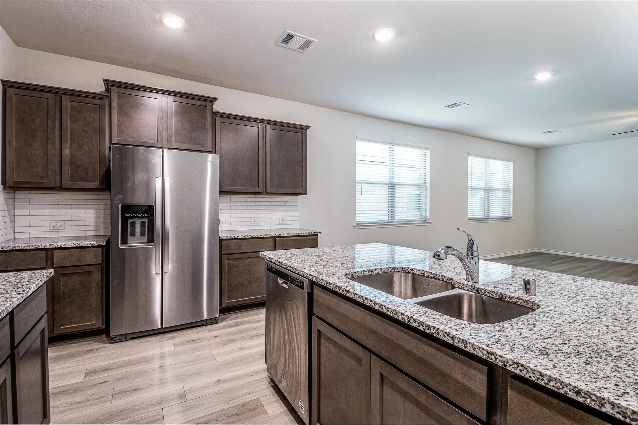 Kitchen featuring dark wood-finish cabinetry, stainless steel appliances, granite countertops, white subway tile backsplash, and wood-finish flooring