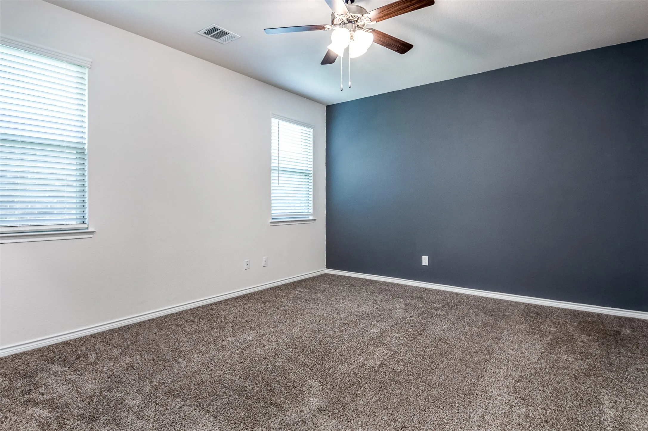 Carpeted flooring, two windows with blinds, ceiling fan with light fixture, white and accent wall finishes