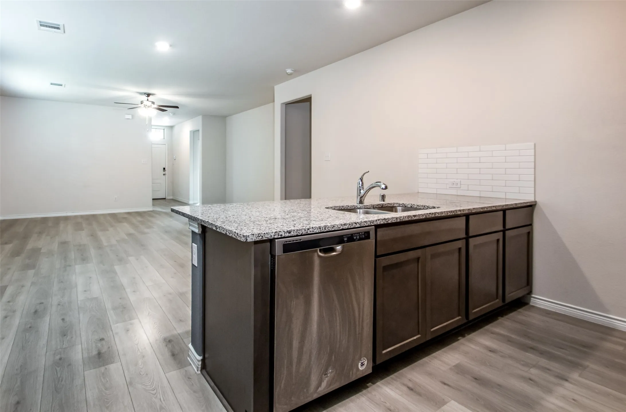 Kitchen island with a stainless steel sink, chrome faucet, stone countertop, and subway tile backsplash