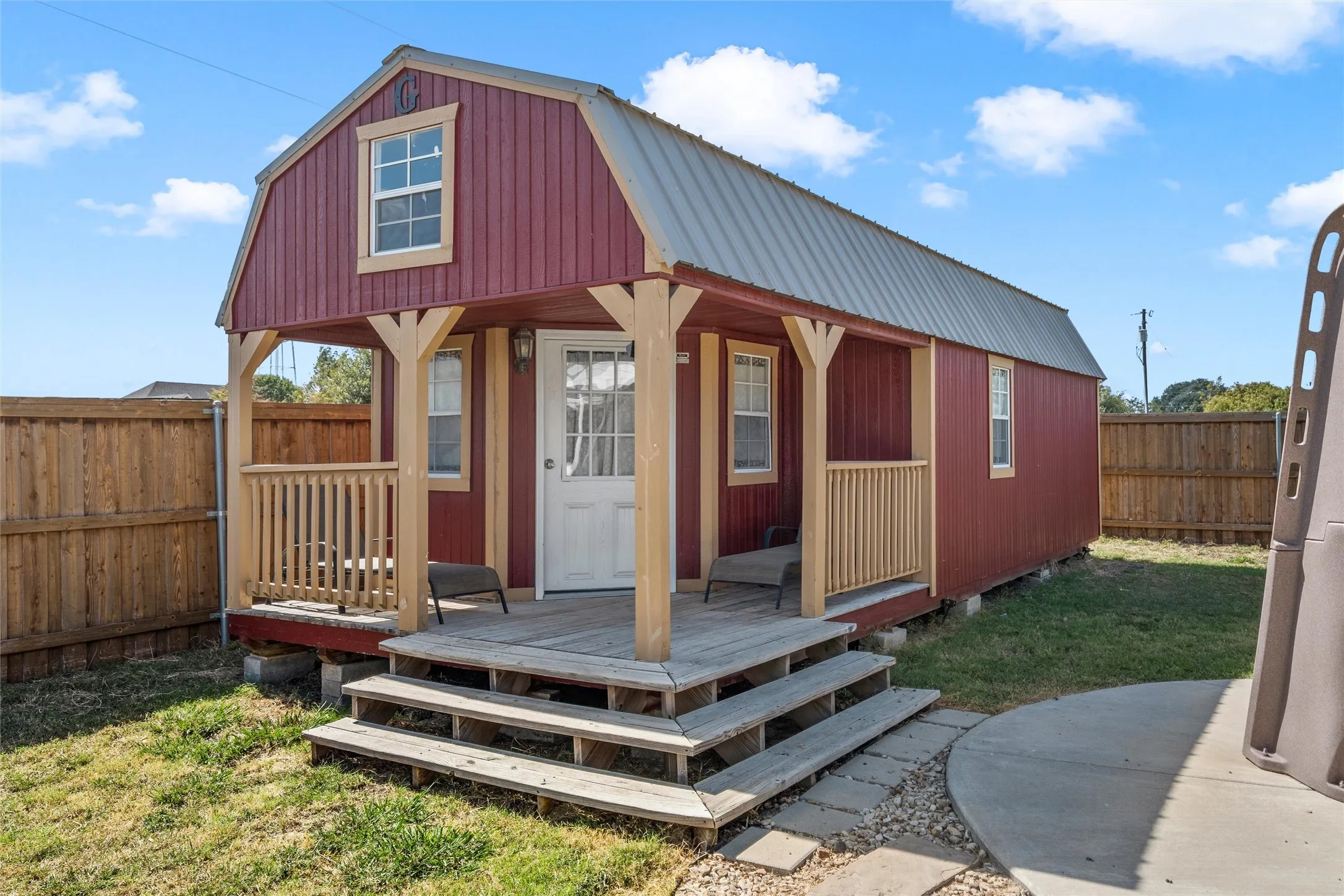 Red-sided structure featuring a covered porch, wood-plank steps, and a metal gambrel roof