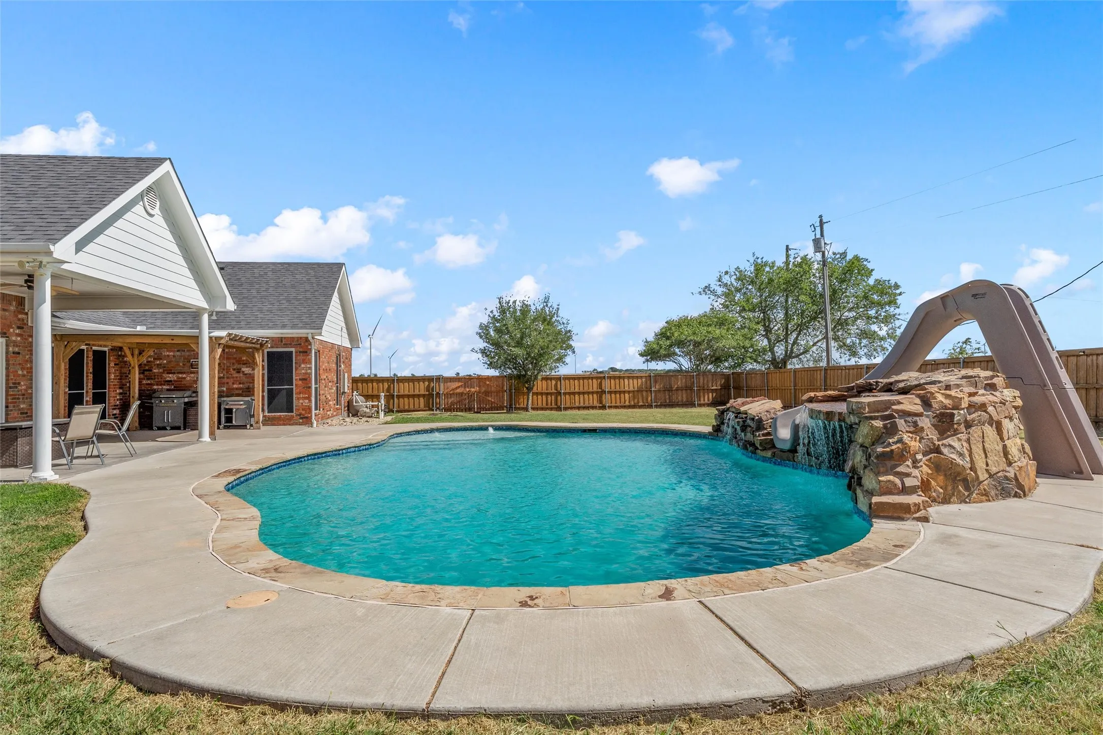 In-ground swimming pool with a rock waterfall feature and attached slide
