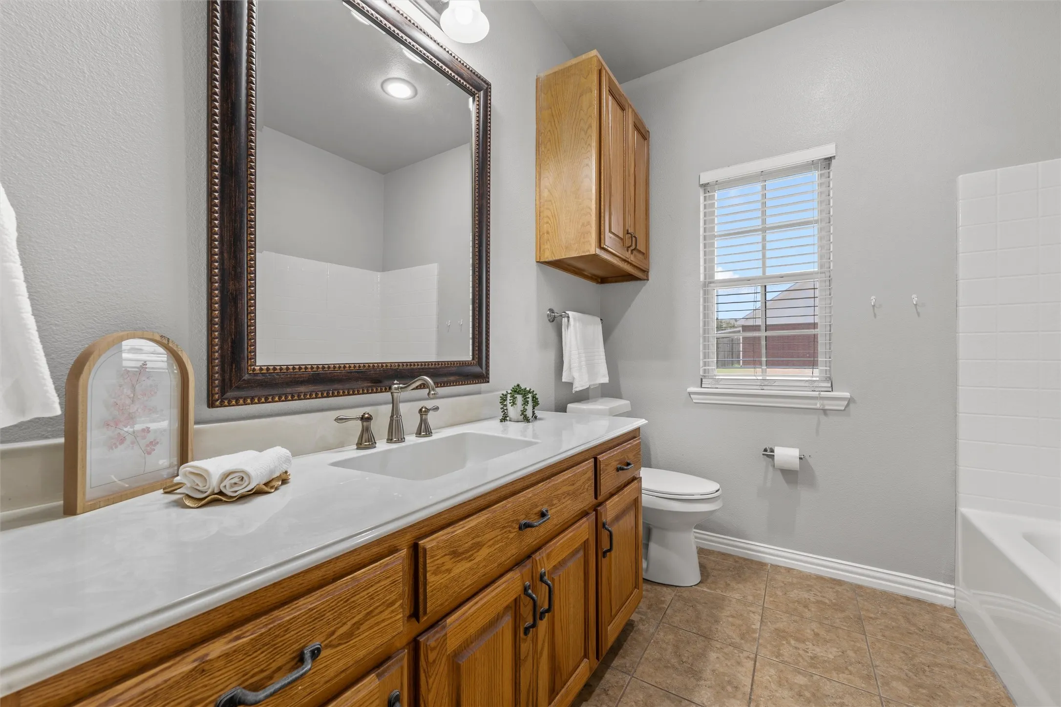 Extended vanity with a white countertop, wood finish cabinetry, and a large framed mirror