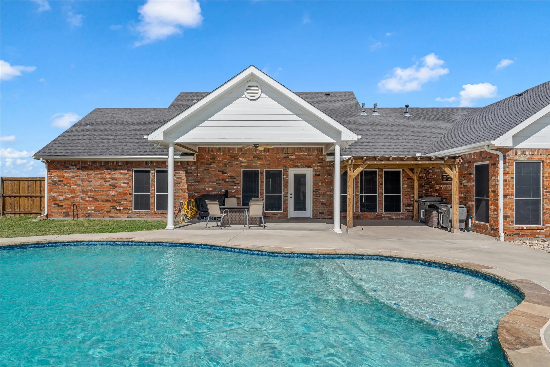Brick exterior, covered patio, outdoor pergola, and an in-ground swimming pool