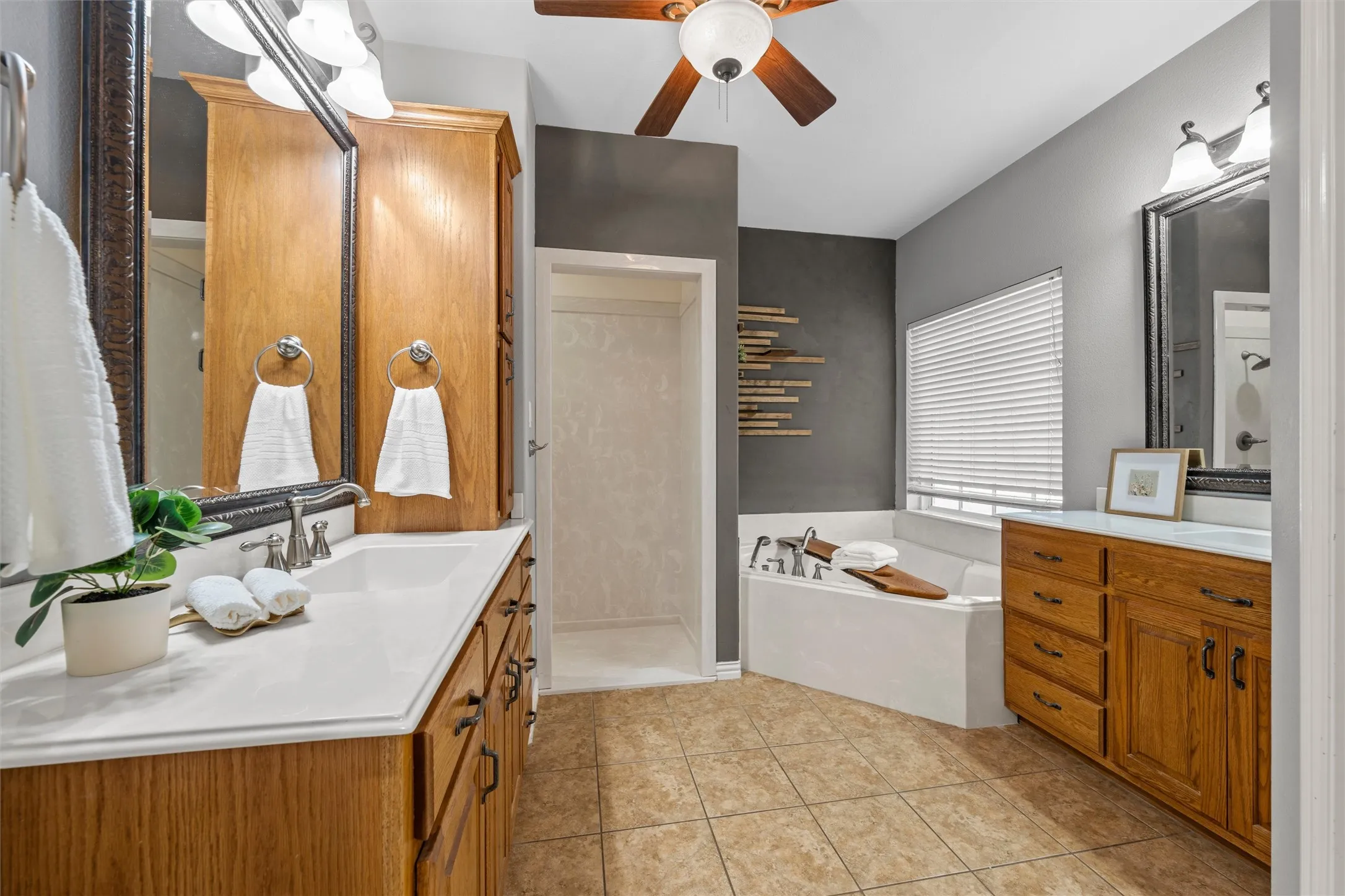 Dual wood-finish vanities with solid surface countertops, a built-in soaking tub, and a separate shower enclosure