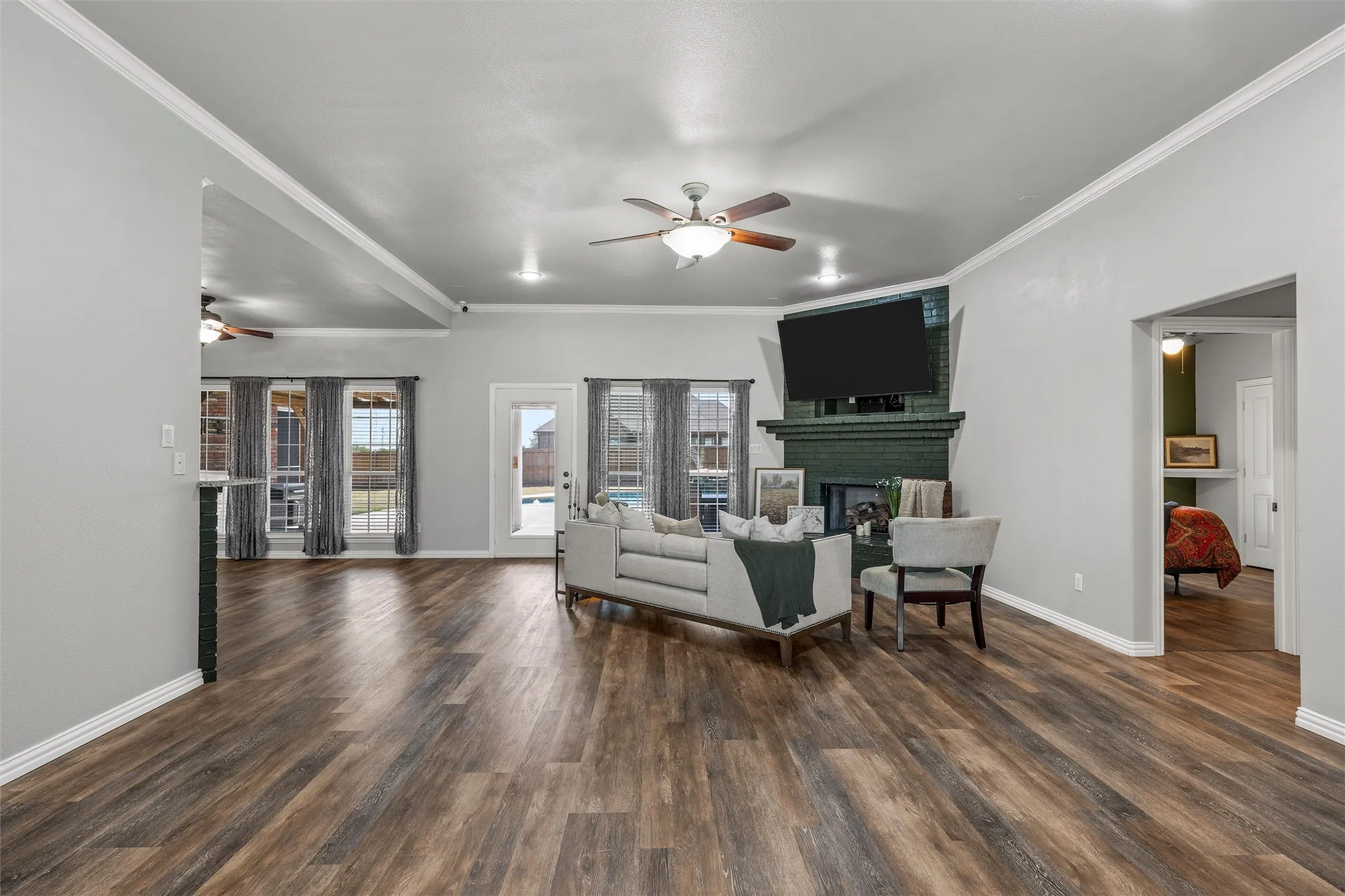 Spacious open-concept living area featuring wood-finish flooring, a ceiling fan, and multiple large windows with exterior pool views