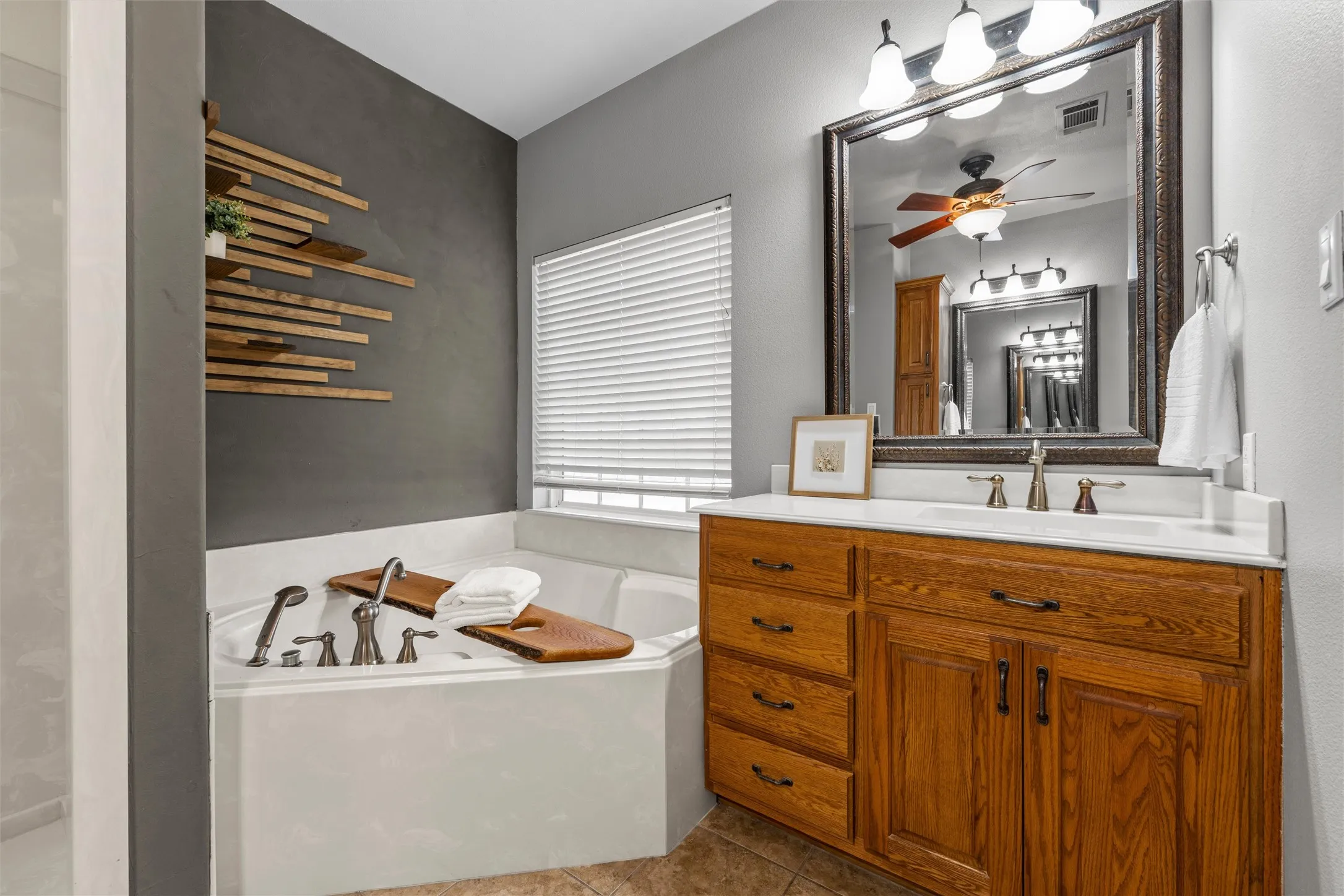 Built-in soaking tub with brushed nickel fixtures, wood-finish vanity with a white countertop, and a large framed mirror with integrated lighting