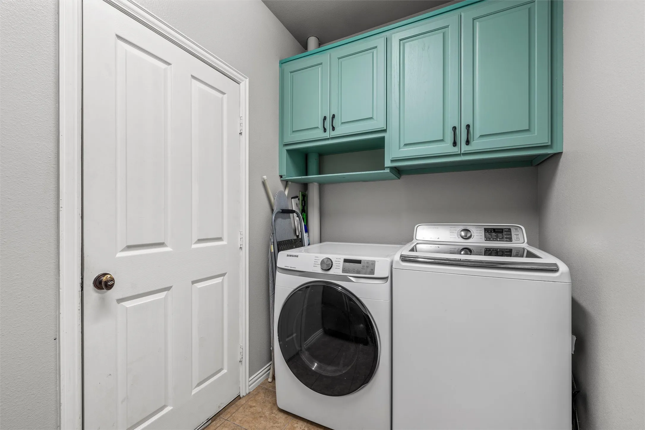 Laundry area featuring overhead cabinetry, an open storage shelf, and tile flooring