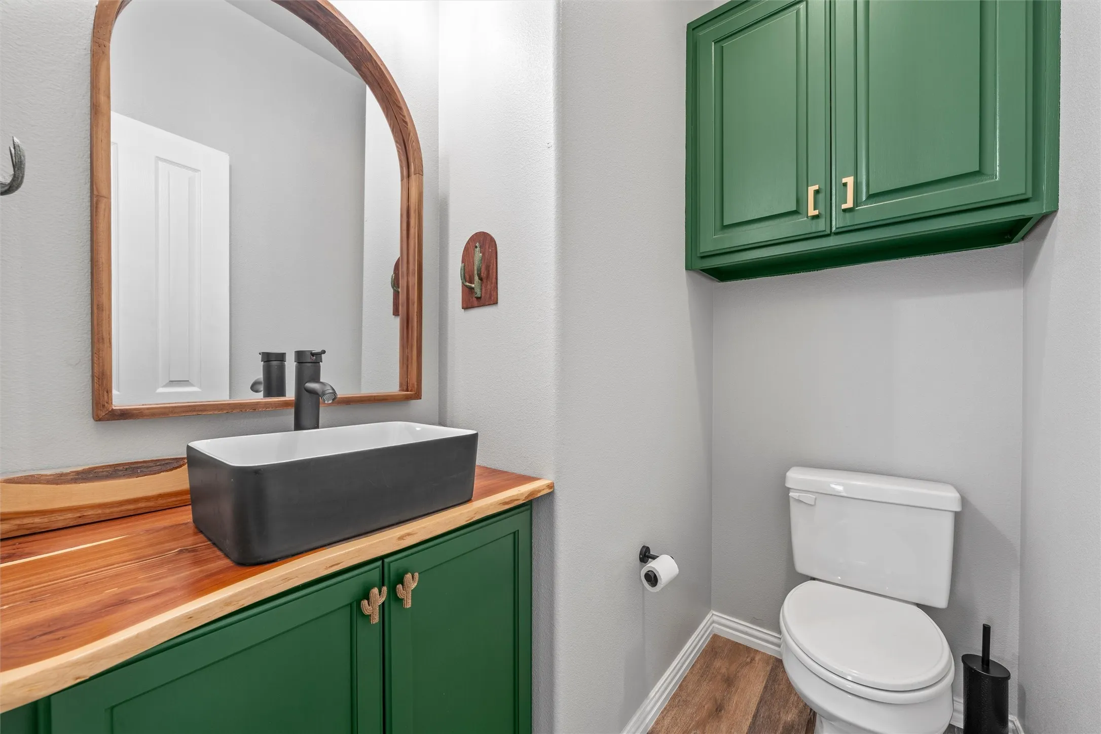 Green cabinetry, wood-finish countertop, matte black vessel sink, matte black faucet, and wood-finish flooring