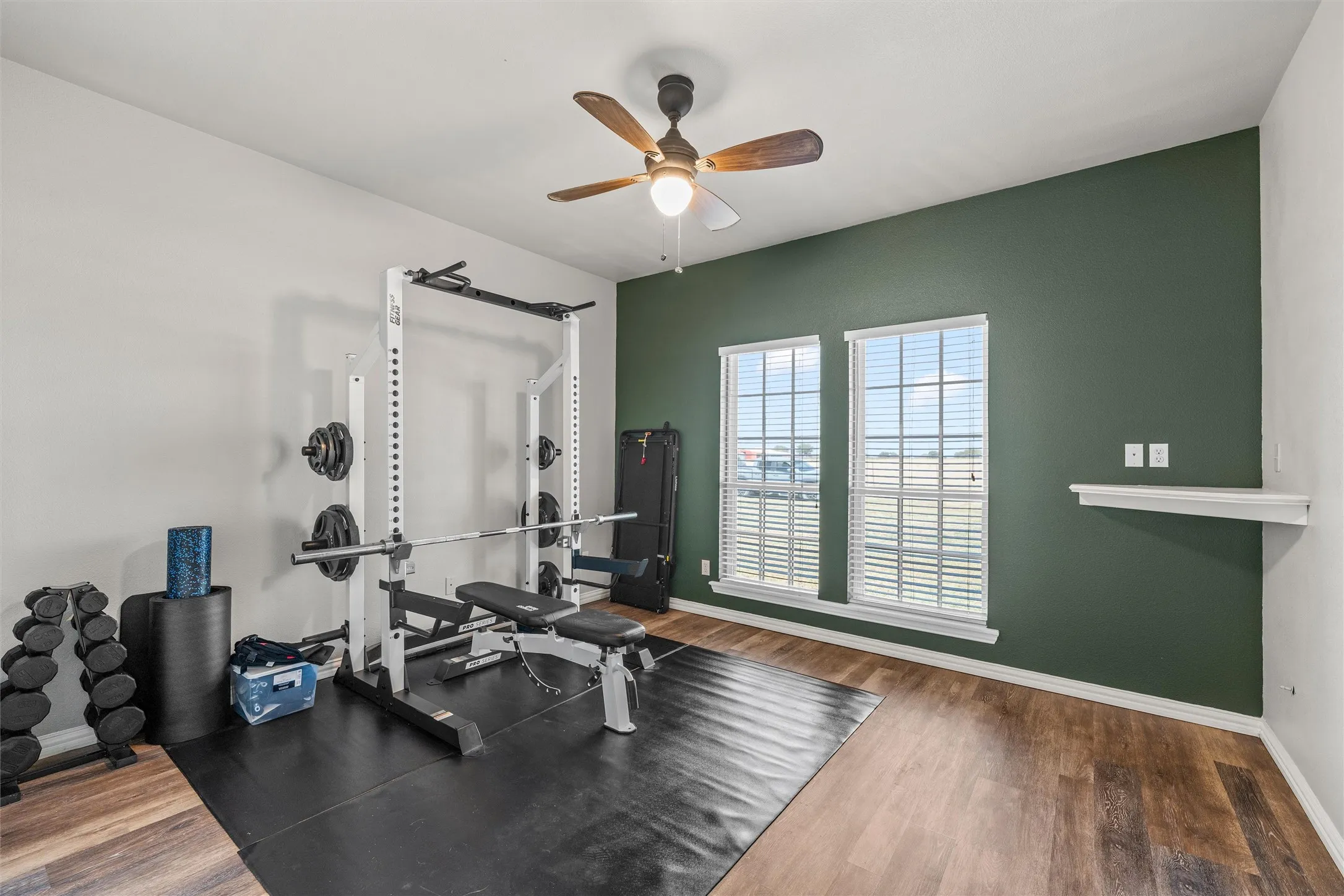 Spacious room featuring wood-finish flooring, a ceiling fan, and two windows with blinds