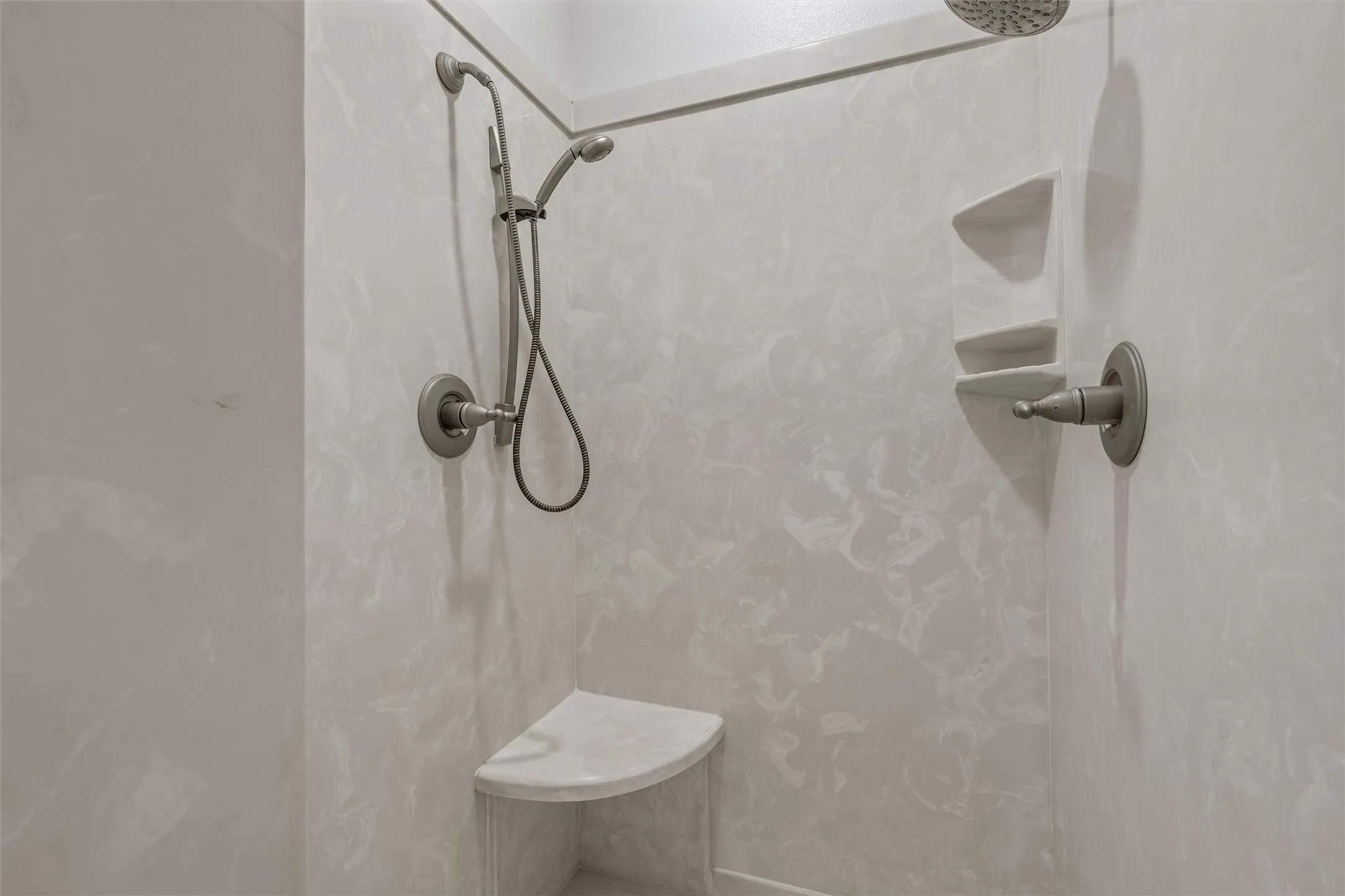 Shower stall with a built-in bench, integrated shelving, a handheld shower fixture, and a standard shower head