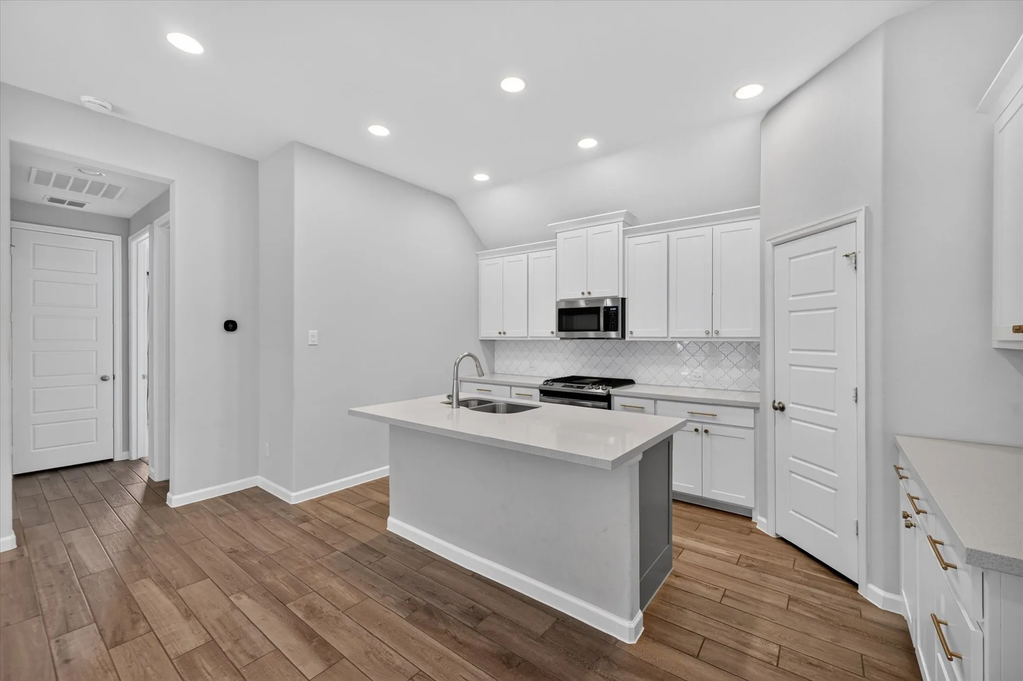 Modern kitchen featuring white cabinetry, stainless steel appliances, a white tile backsplash, a central island with a sink, and wood-finish flooring