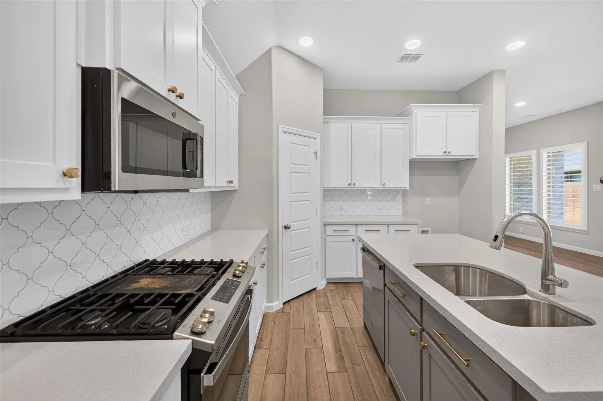 Kitchen featuring white shaker cabinetry, stainless steel appliances, light-toned countertops, and wood-finish flooring