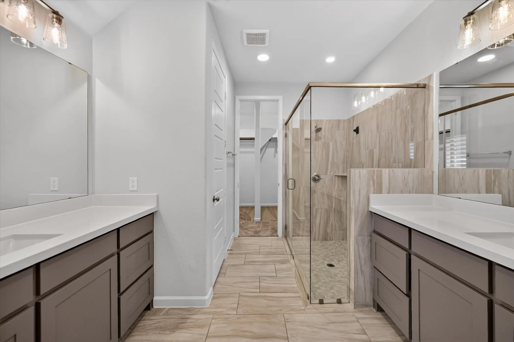 Dual vanities with white countertops, a frameless glass shower enclosure, wood-finish flooring, and recessed lighting