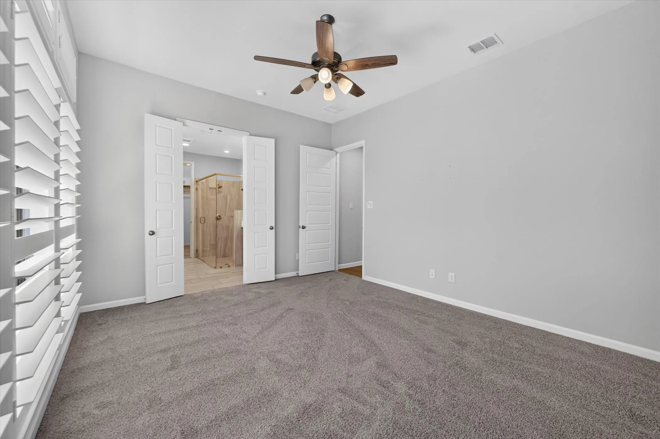 Carpeted room with a ceiling fan, white paneled doors, and plantation shutters