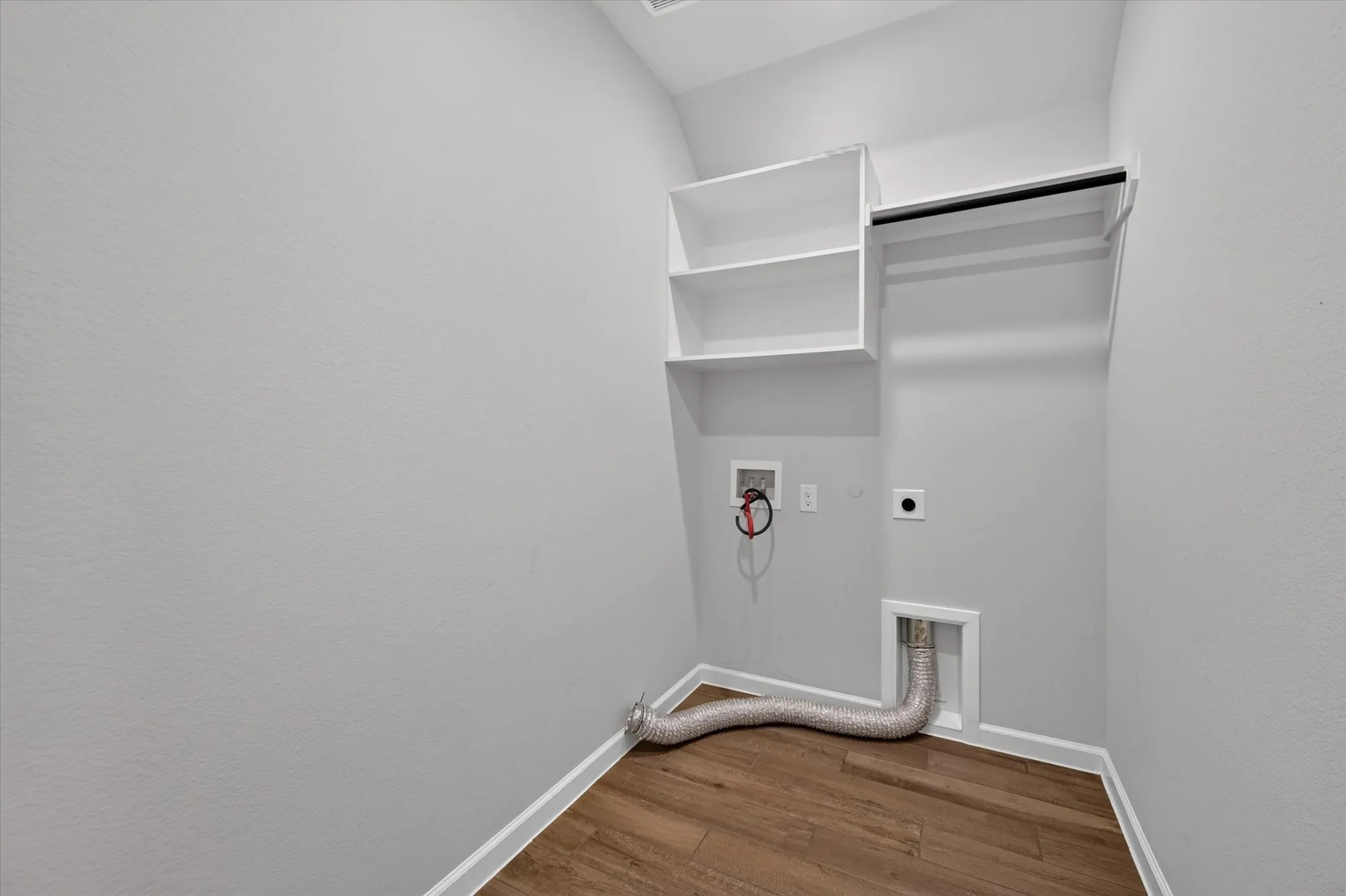 Laundry area featuring wood-finish flooring, white built-in shelving, and a garment rod