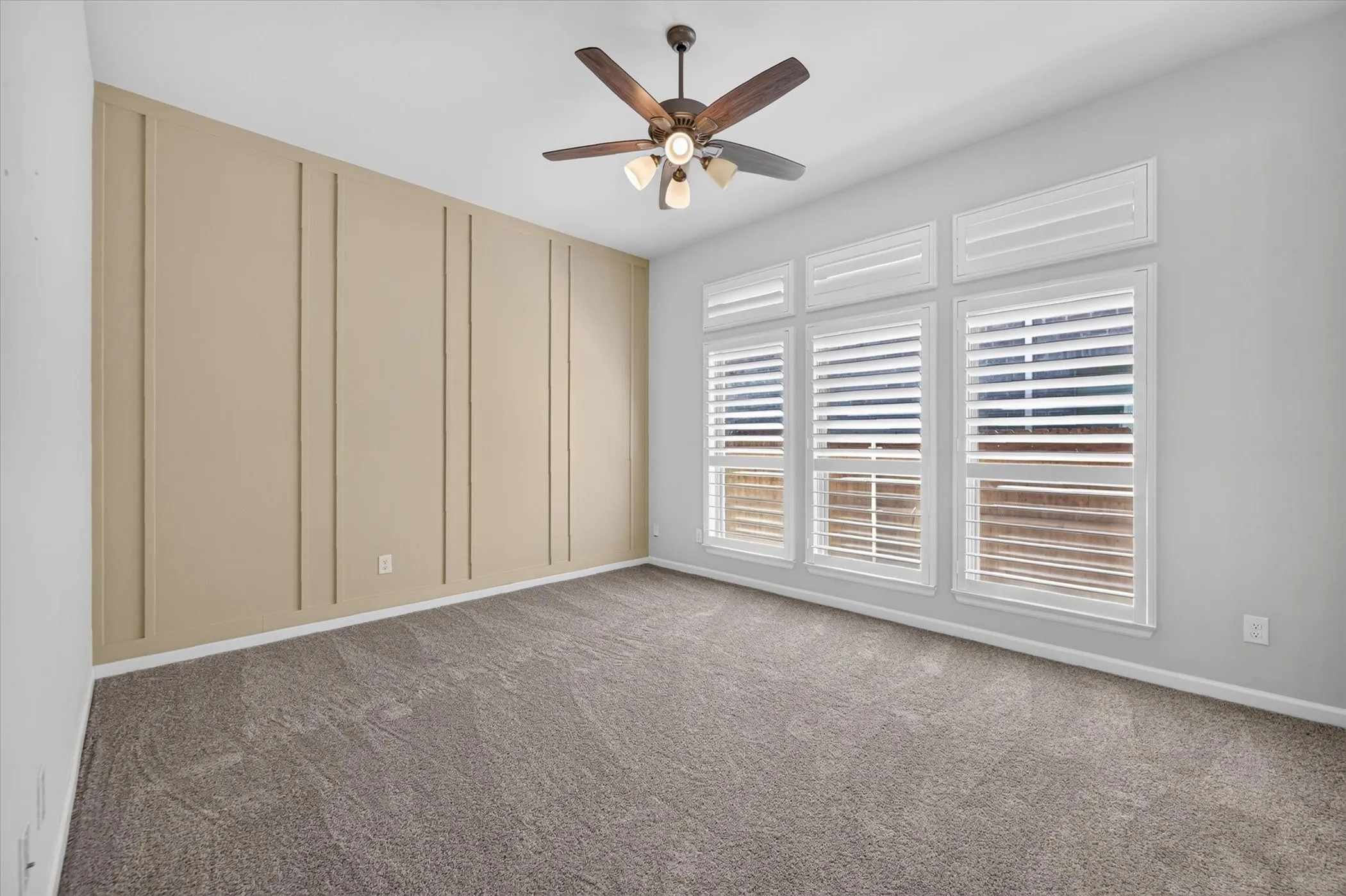 Spacious bedroom with neutral carpet flooring, ceiling fan with integrated lighting, and expansive wall of built-in cabinetry featuring vertical paneling