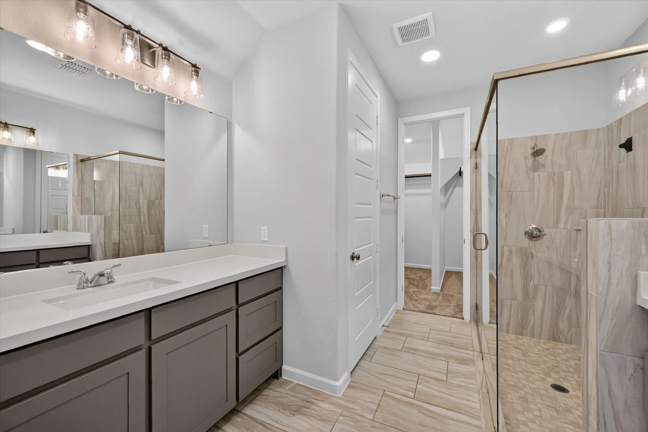 Spa-inspired primary bathroom featuring a dual-sink vanity with wood cabinetry, white quartz countertops, and polished nickel fixtures
