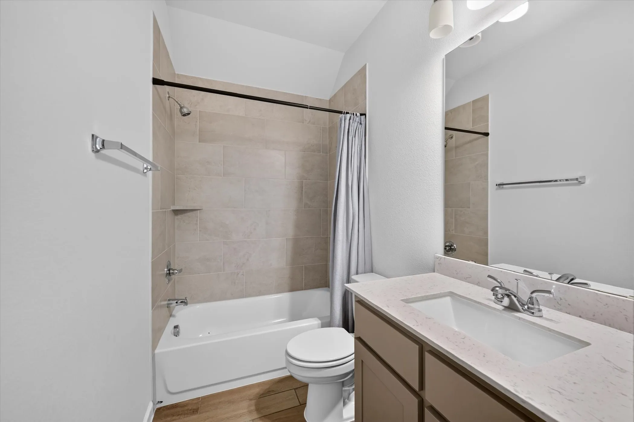 Bathroom featuring a built-in tub with tile surround, wood-finish flooring, a vanity with an integrated sink, a large mirror, and overhead lighting