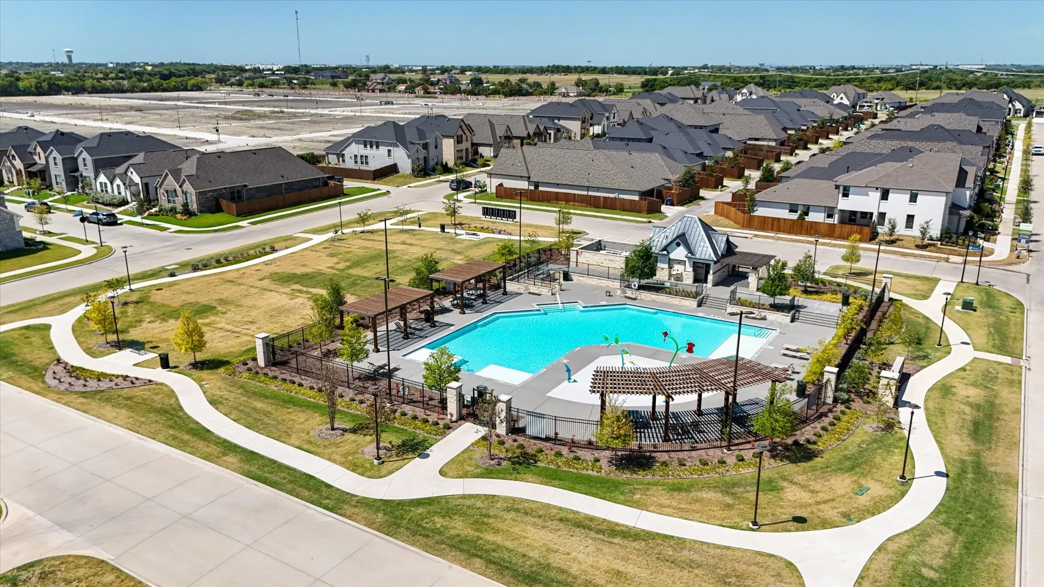 Community swimming pool with sun shelf, adjacent pool deck with pergolas, and a separate splash pad