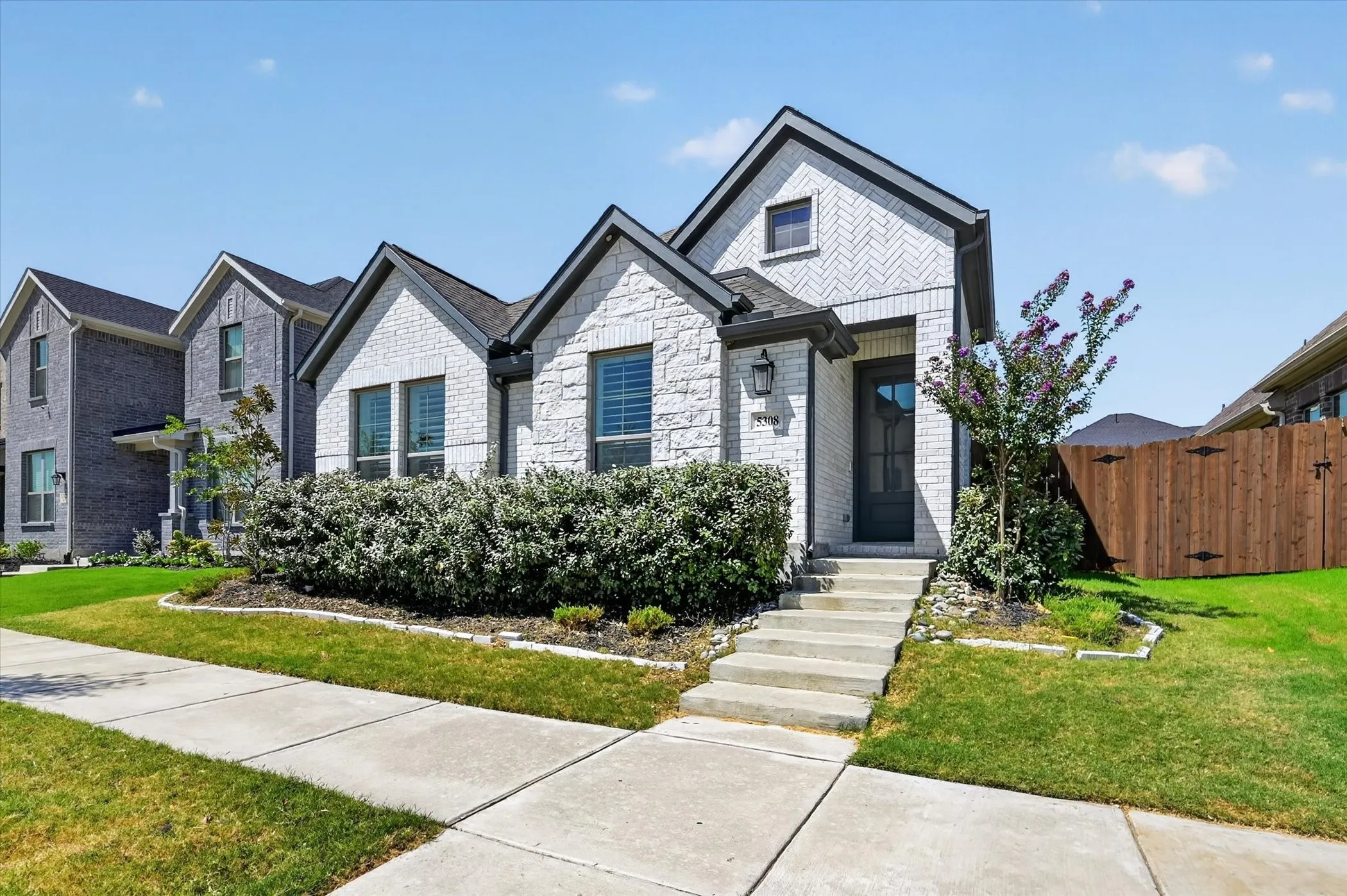 White brick exterior with dark trim accents, concrete front walkway, landscaped front yard, and dark-paneled front door