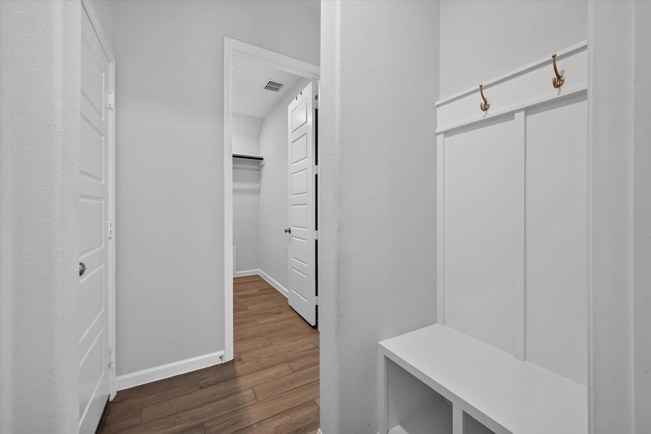 Built-in storage bench with coat hooks, wood-finish flooring, and white paneled doors