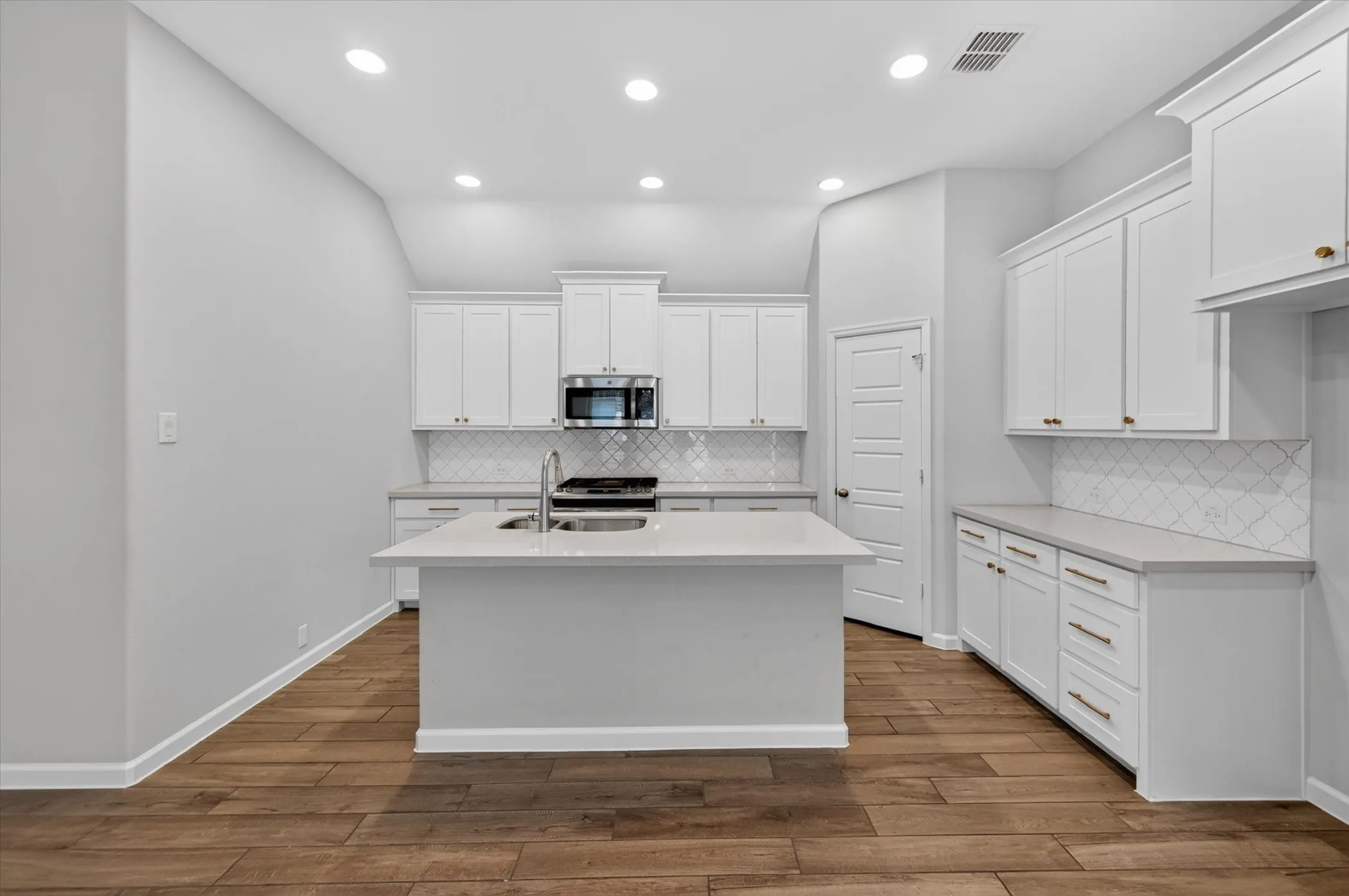Kitchen featuring an island with an undermount sink, white cabinetry, stainless steel microwave, and wood-finish flooring