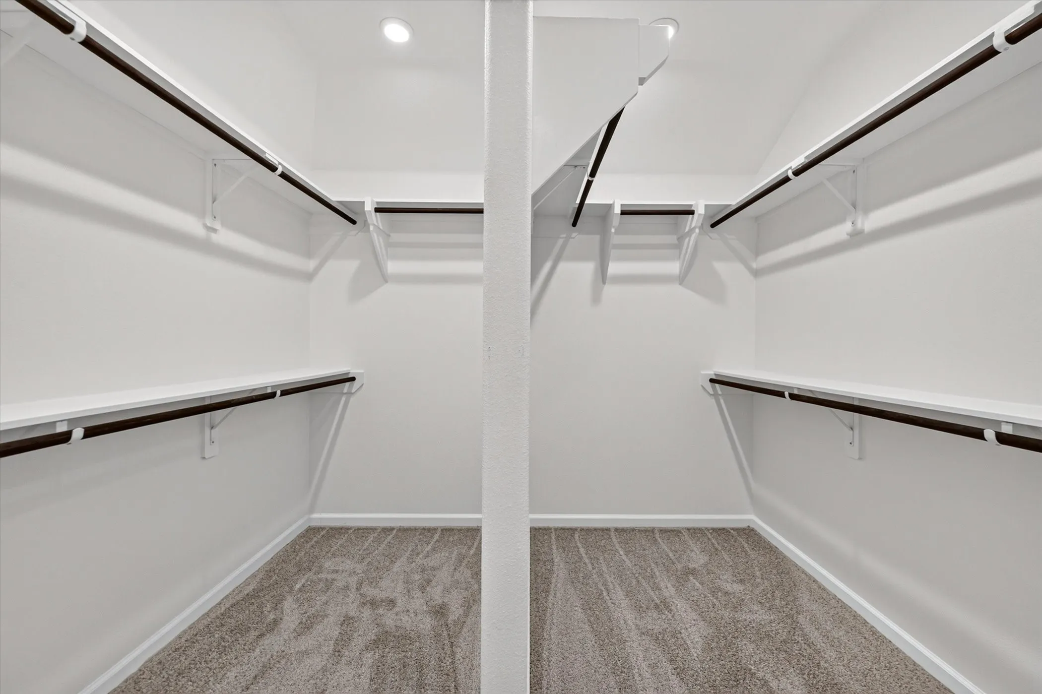 Recessed lighting illuminating a walk-in closet featuring built-in shelving, hanging rods, and carpeting