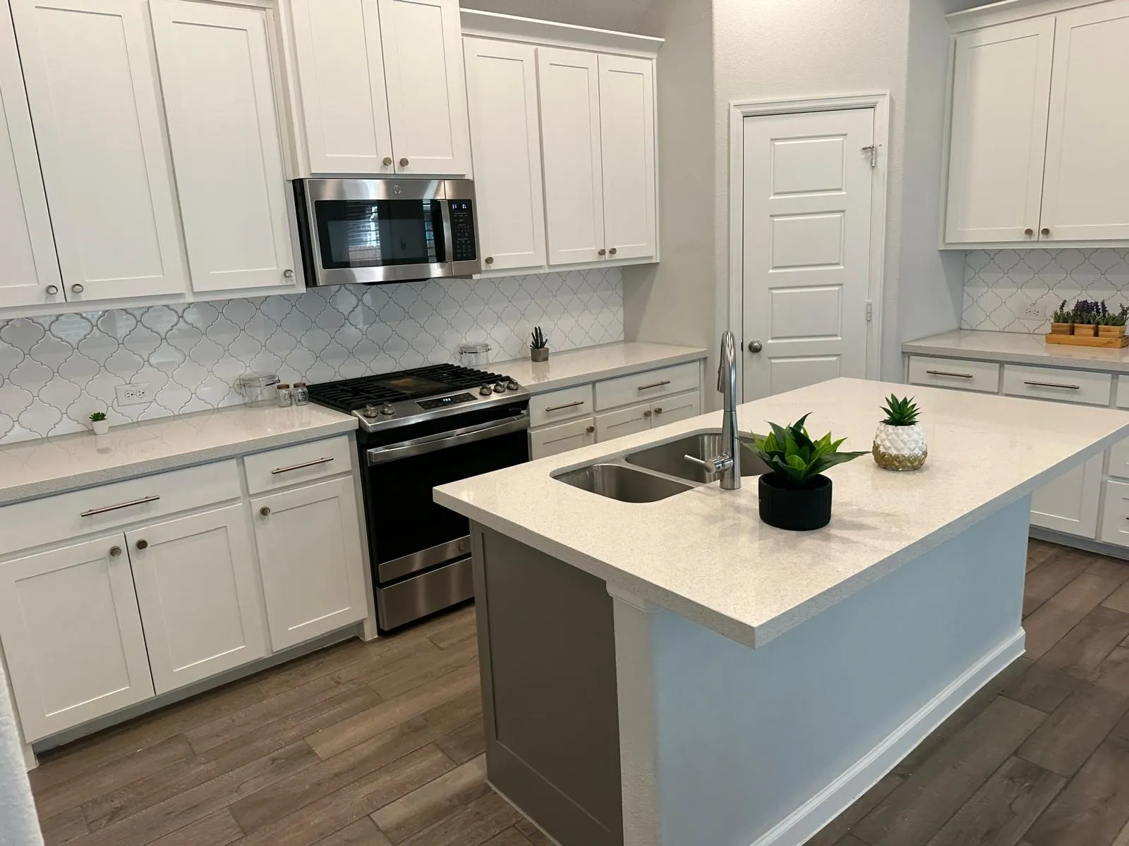 Kitchen featuring white shaker cabinetry, stainless steel appliances, patterned tile backsplash, light-toned countertops, and wood-finish flooring