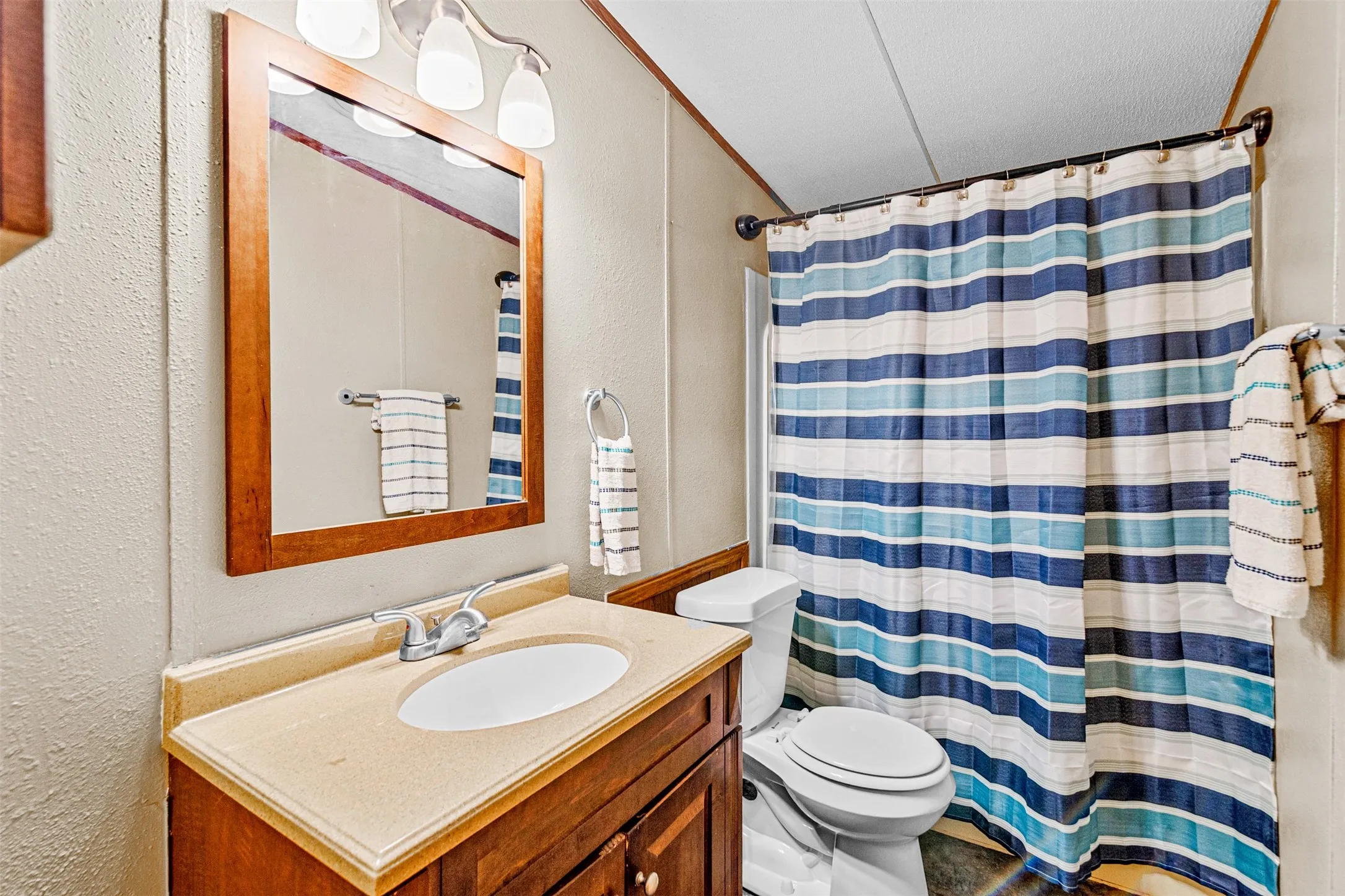 Bathroom featuring a wood-finish vanity with an integrated sink, a framed mirror, and a wall-mounted light fixture