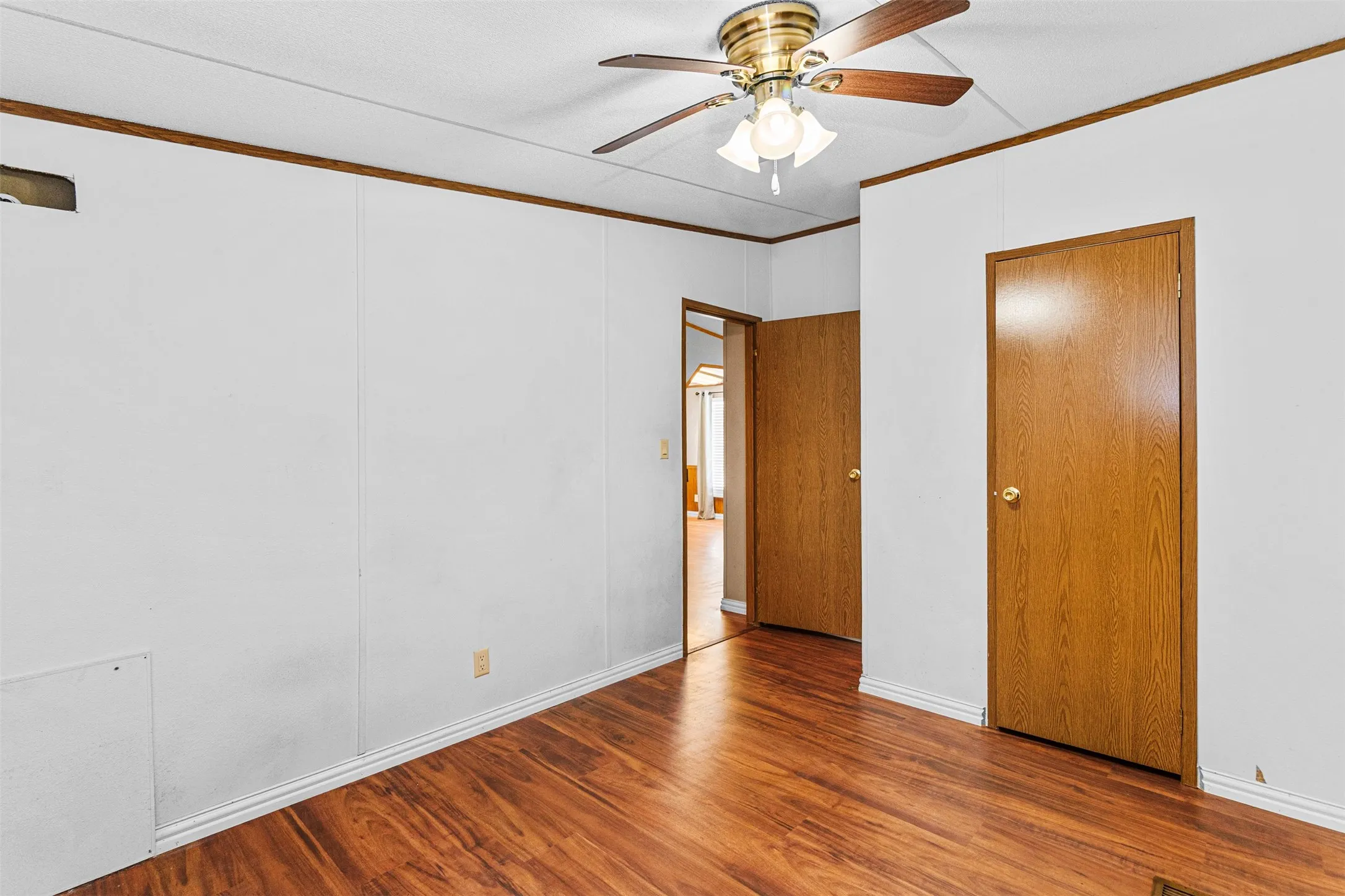 Wood-finish flooring throughout, white paneled walls, and a brass-finish ceiling fan with integrated lighting
