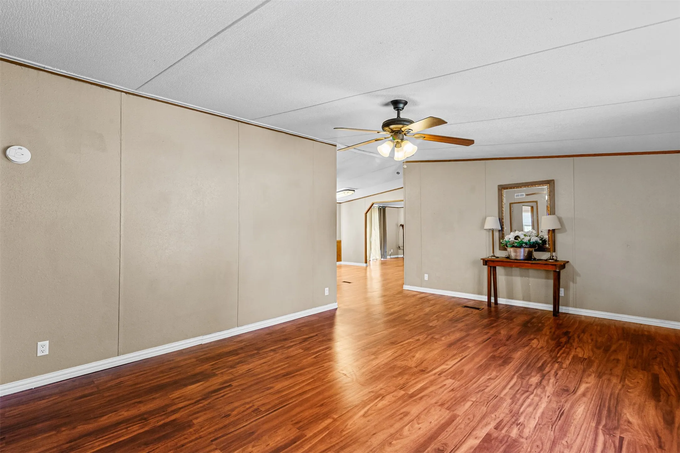 Wood-finish flooring throughout, neutral tone paneled walls, and a ceiling fan with integrated lighting