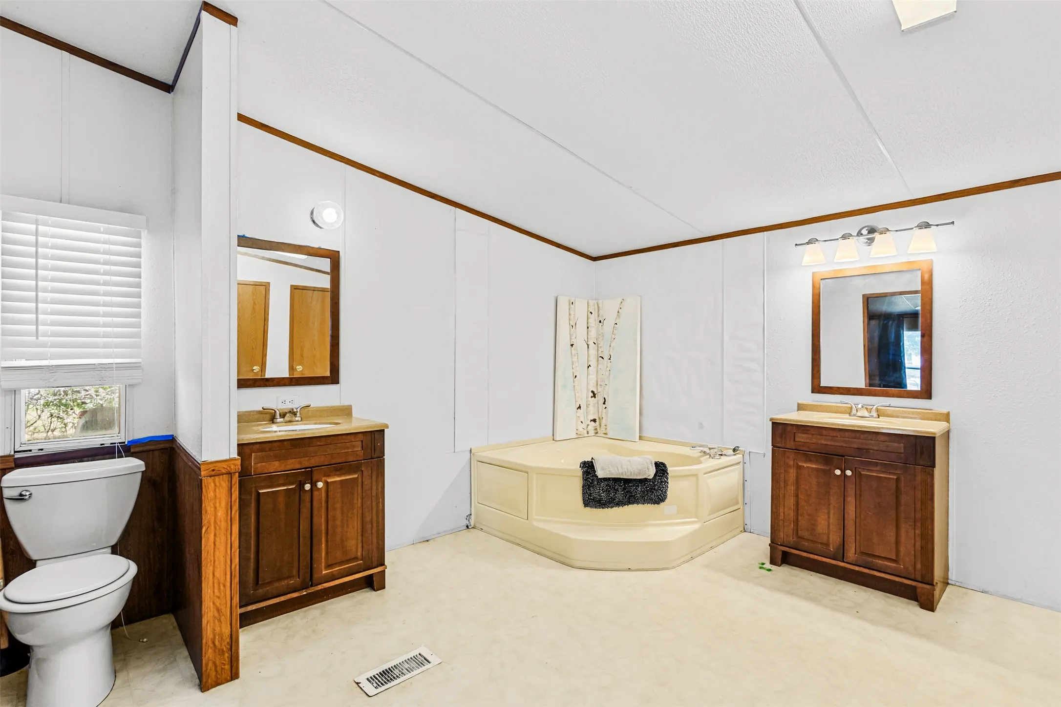 Corner soaking tub, dual vanity sinks with wood cabinetry, and a window with blinds
