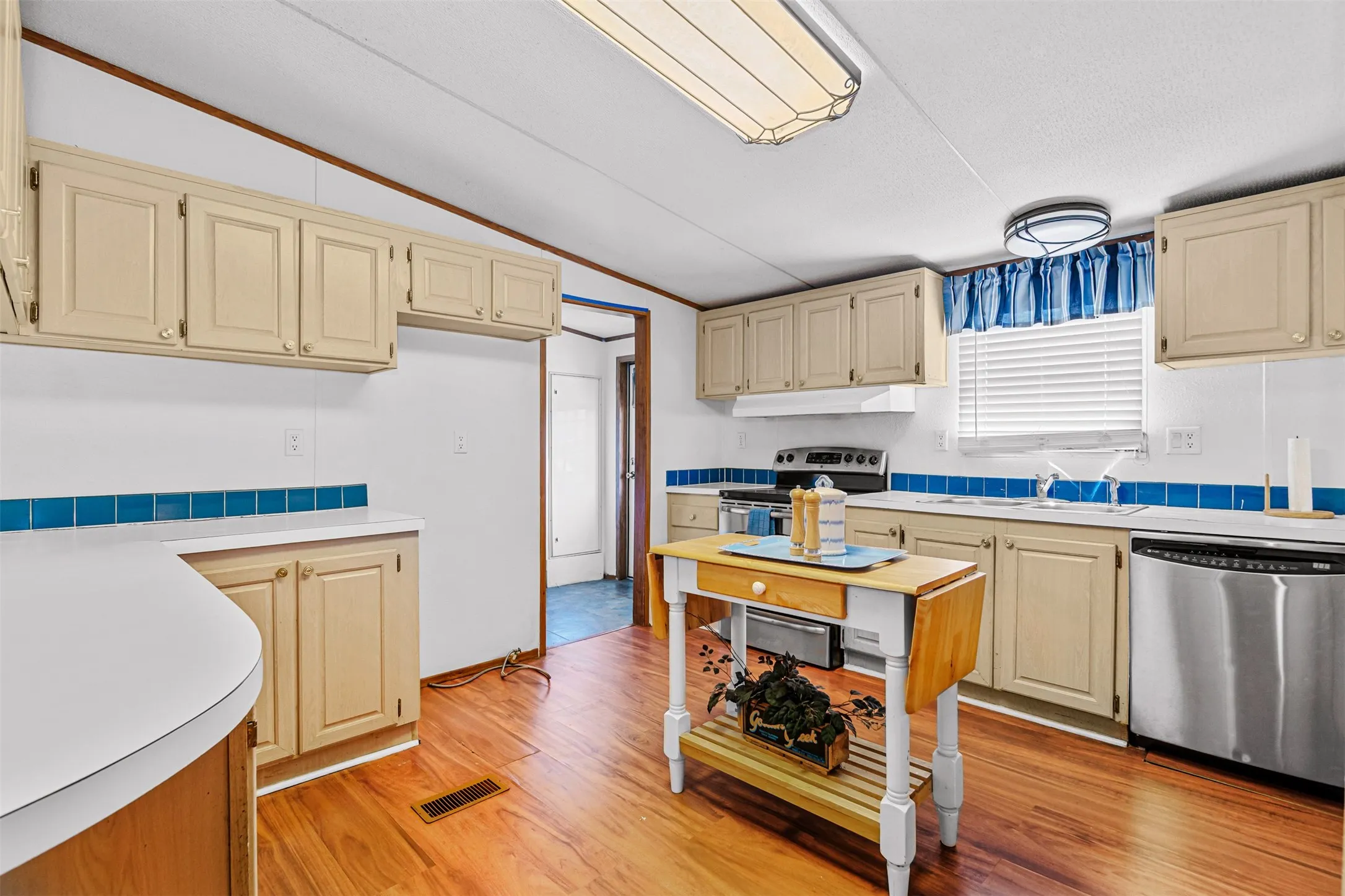 Kitchen featuring wood-finish flooring, cream cabinetry, white countertops, and a blue tile backsplash