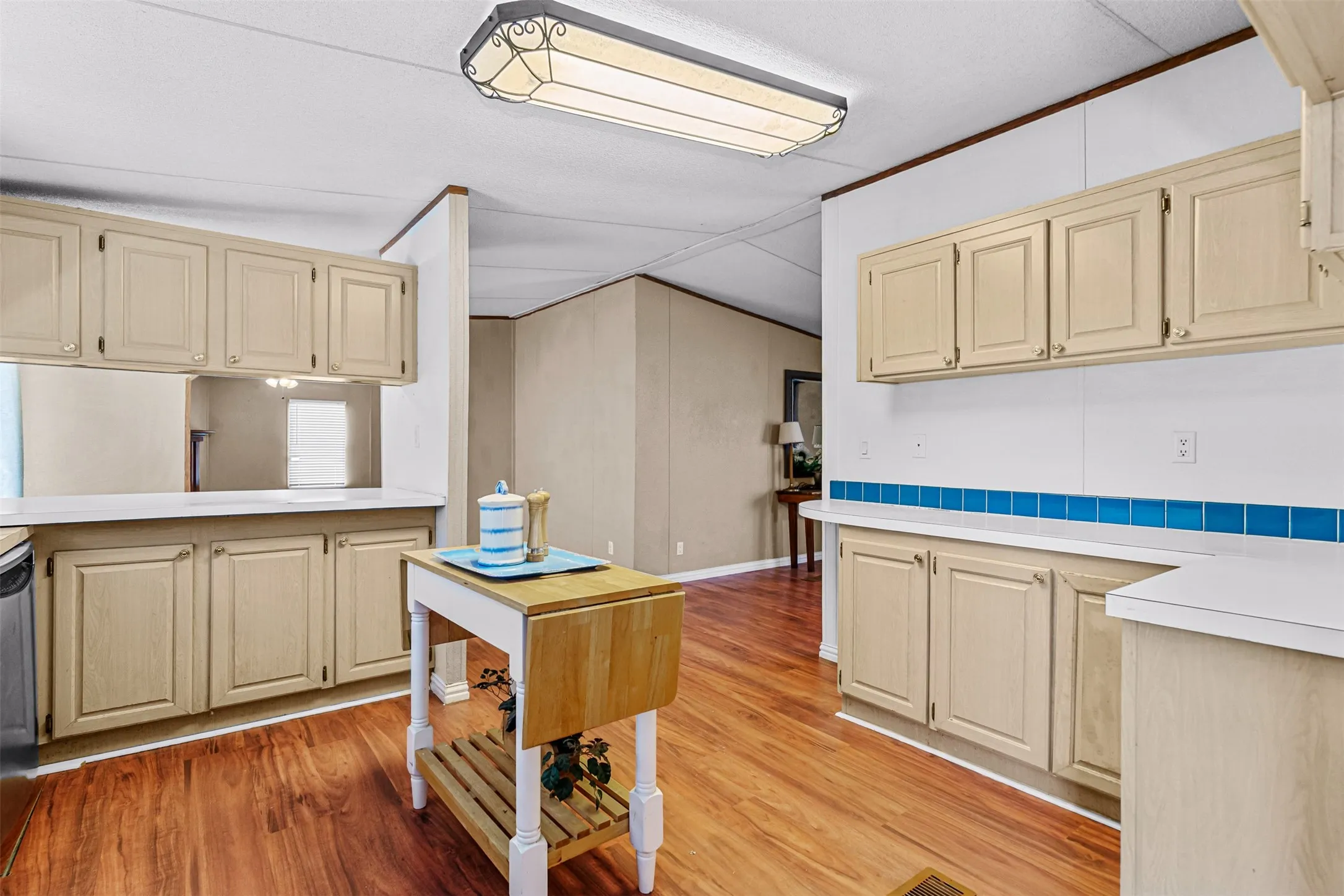 Kitchen featuring wood-finish flooring, light-toned cabinetry, white countertops, and a blue tile backsplash