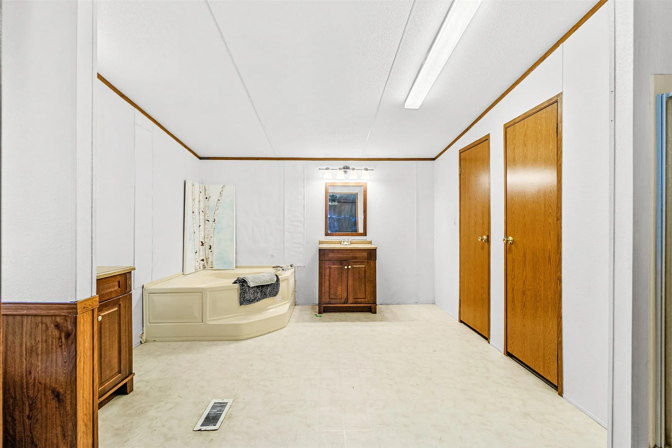 Corner soaking tub, wood-finish vanity with countertop, wall-mounted mirror, and overhead lighting fixture