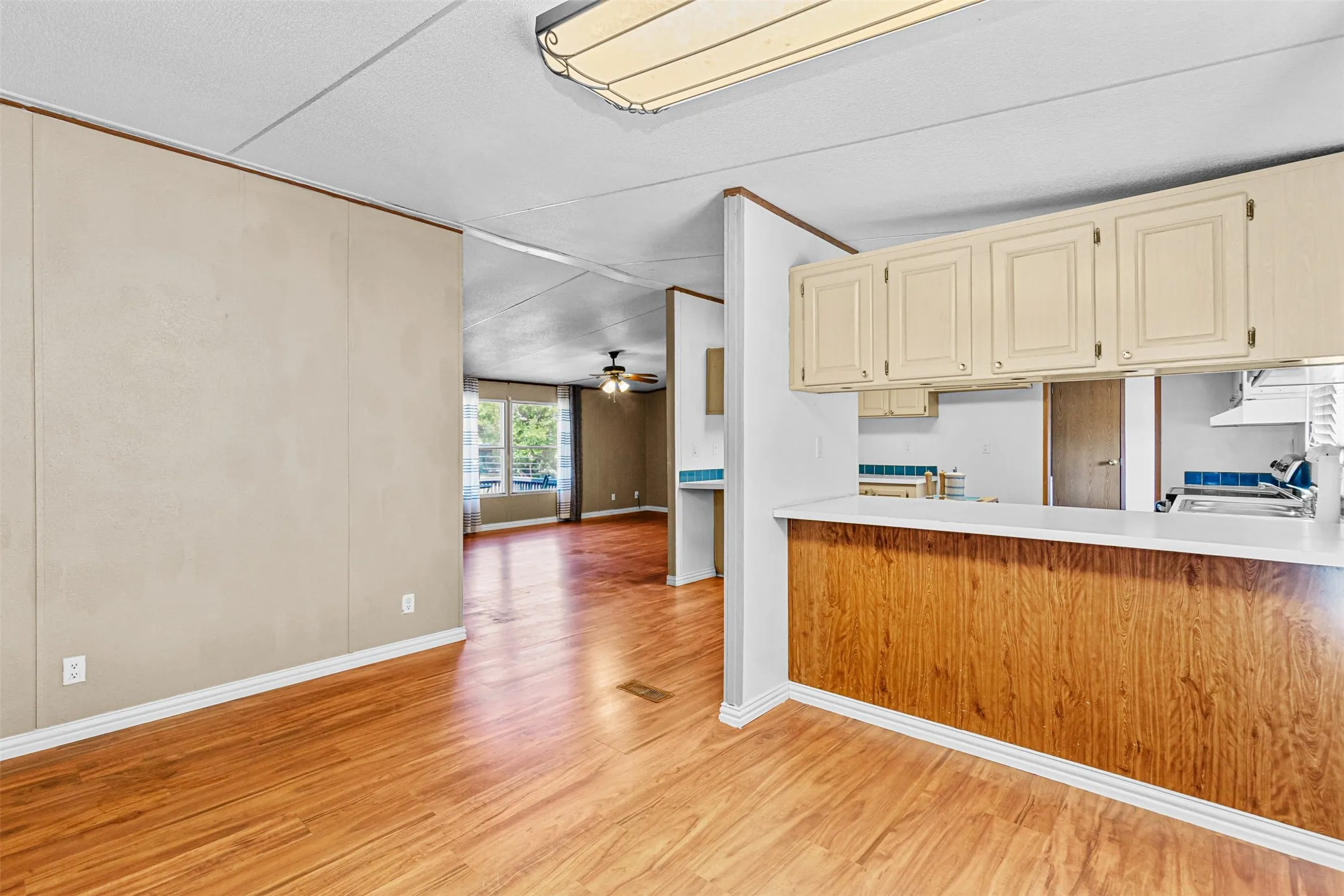 Wood-finish flooring throughout, with a breakfast bar featuring wood paneling and a light-toned countertop