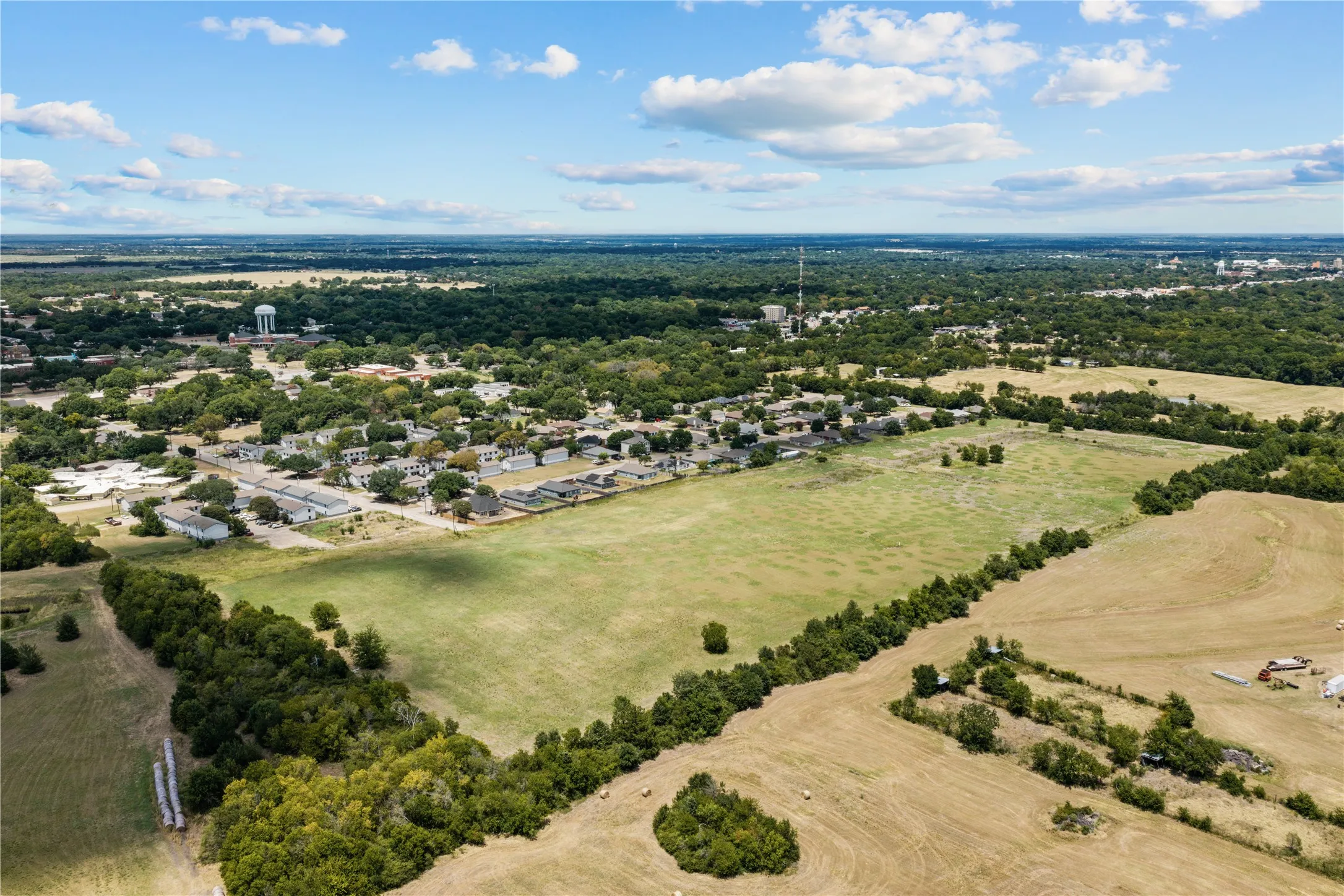 Expansive open land featuring diverse vegetation and distant urban elements