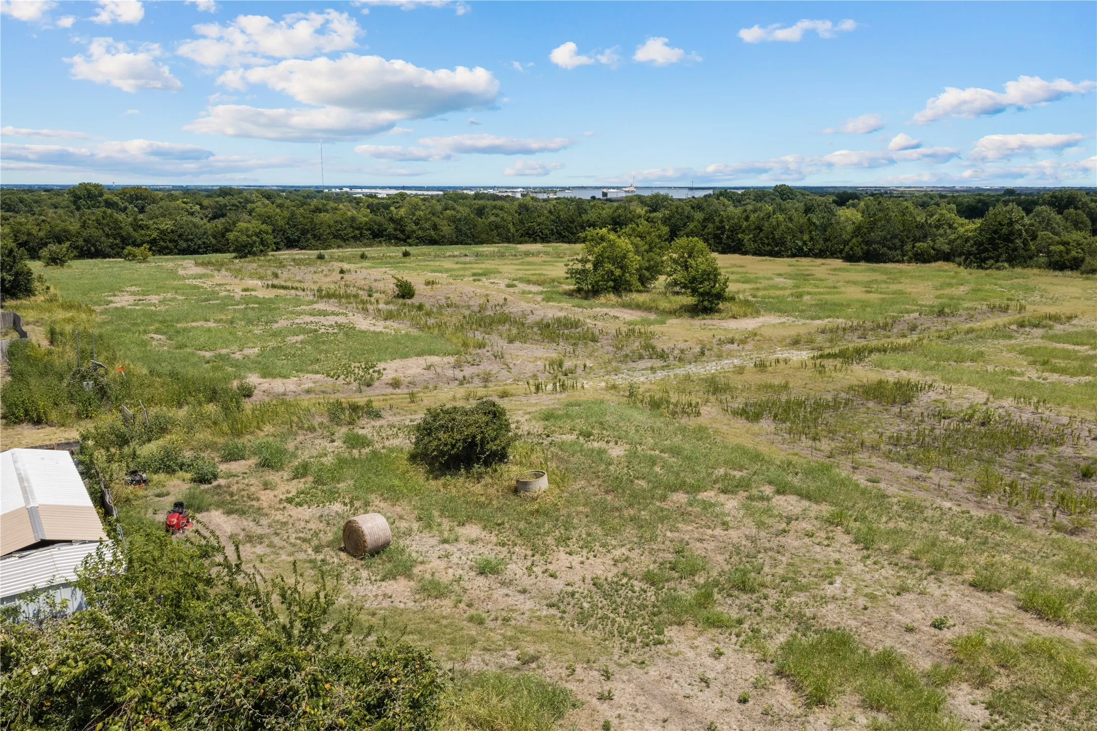 Expansive open land with varied grasses, scattered trees, and distant wooded areas