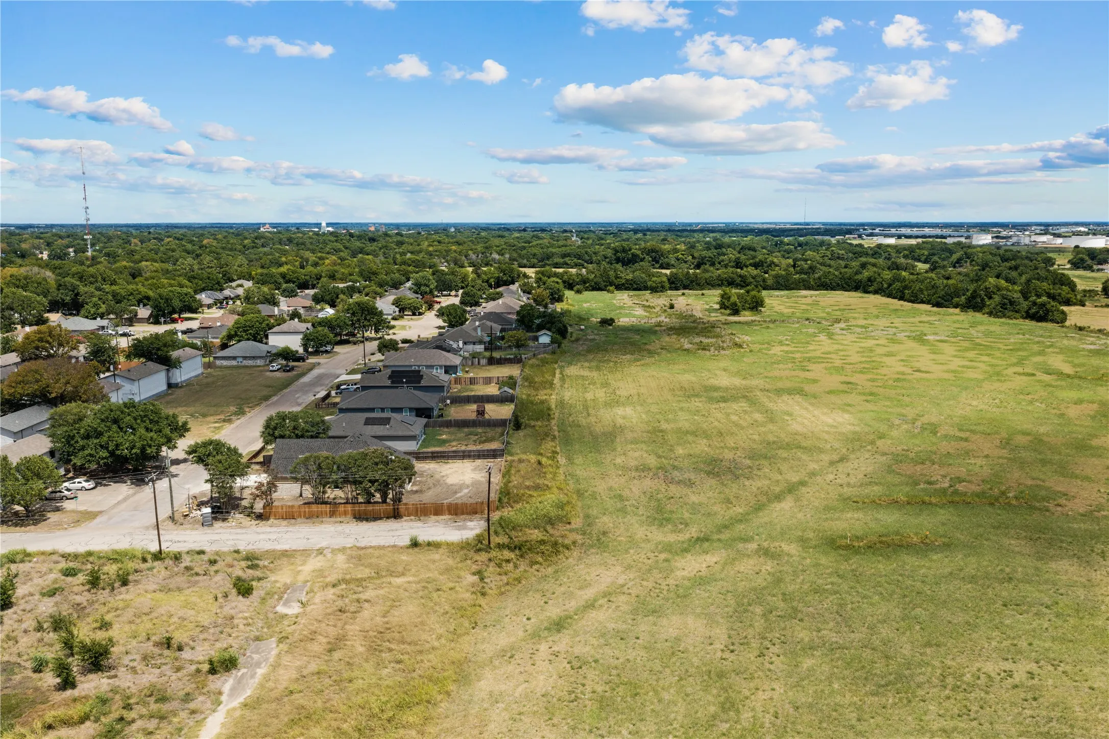 Expansive undeveloped land bordering a residential street with established homes, surrounded by mature trees